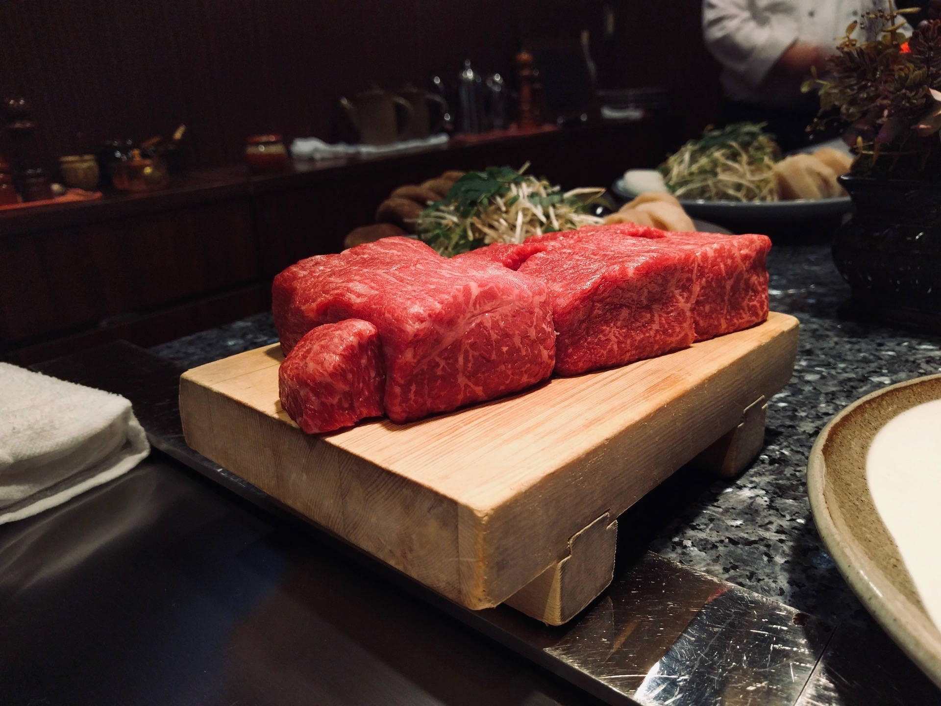 meat 桌布 壁紙 — 兩塊厚切的鮮紅色大理石紋牛肉放在昏暗高級餐廳環境的木板上。