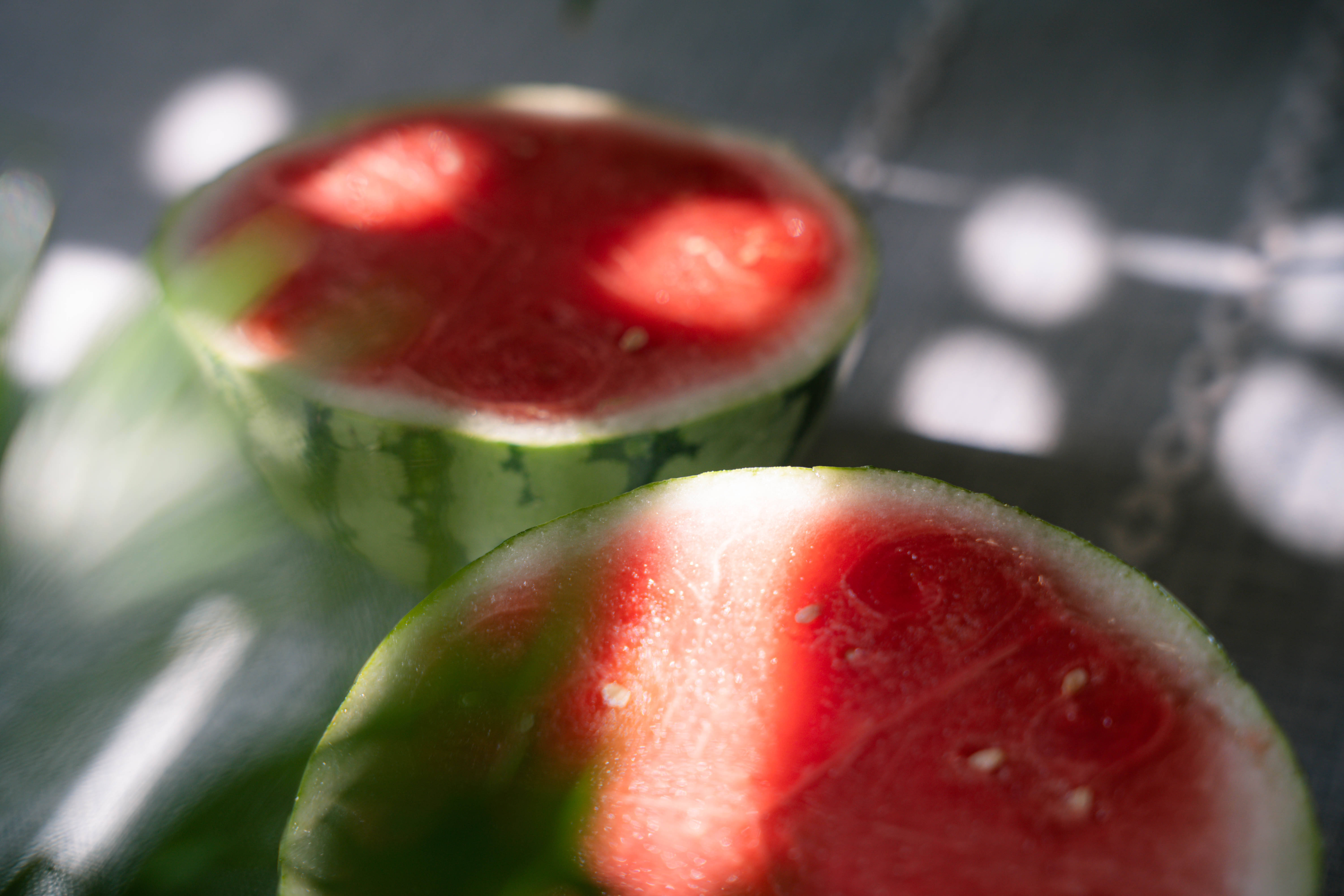 Watermelon 桌布 壁紙 — 兩塊多汁的西瓜半塊在帶有葉影的紋理表面上沐浴斑駁的陽光。