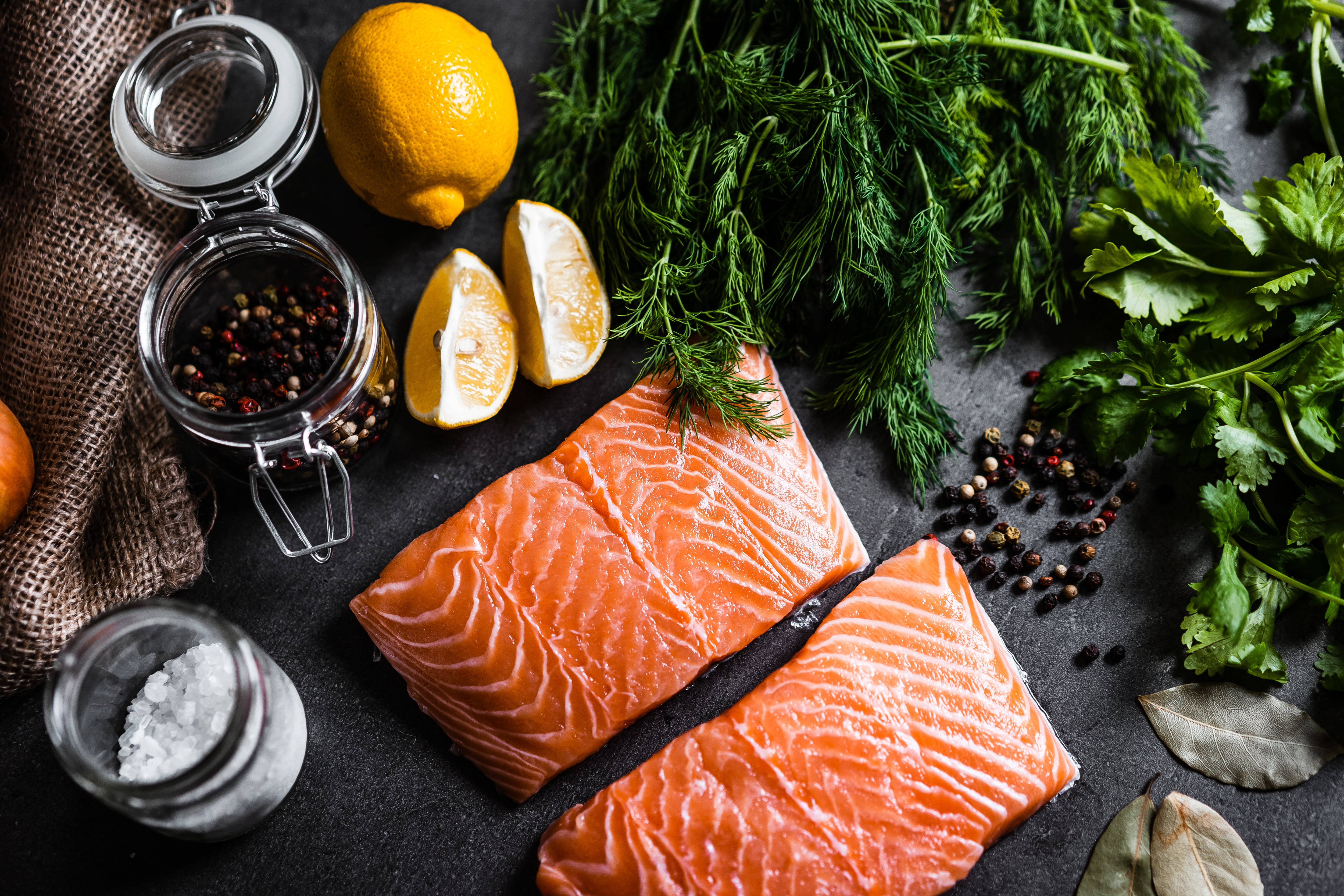 Food Photography 桌布 壁紙 — 兩塊生鮭魚片放在深色石板之上，周圍環繞著新鮮蒔蘿、香菜、檸檬角、胡椒粒和鹽。