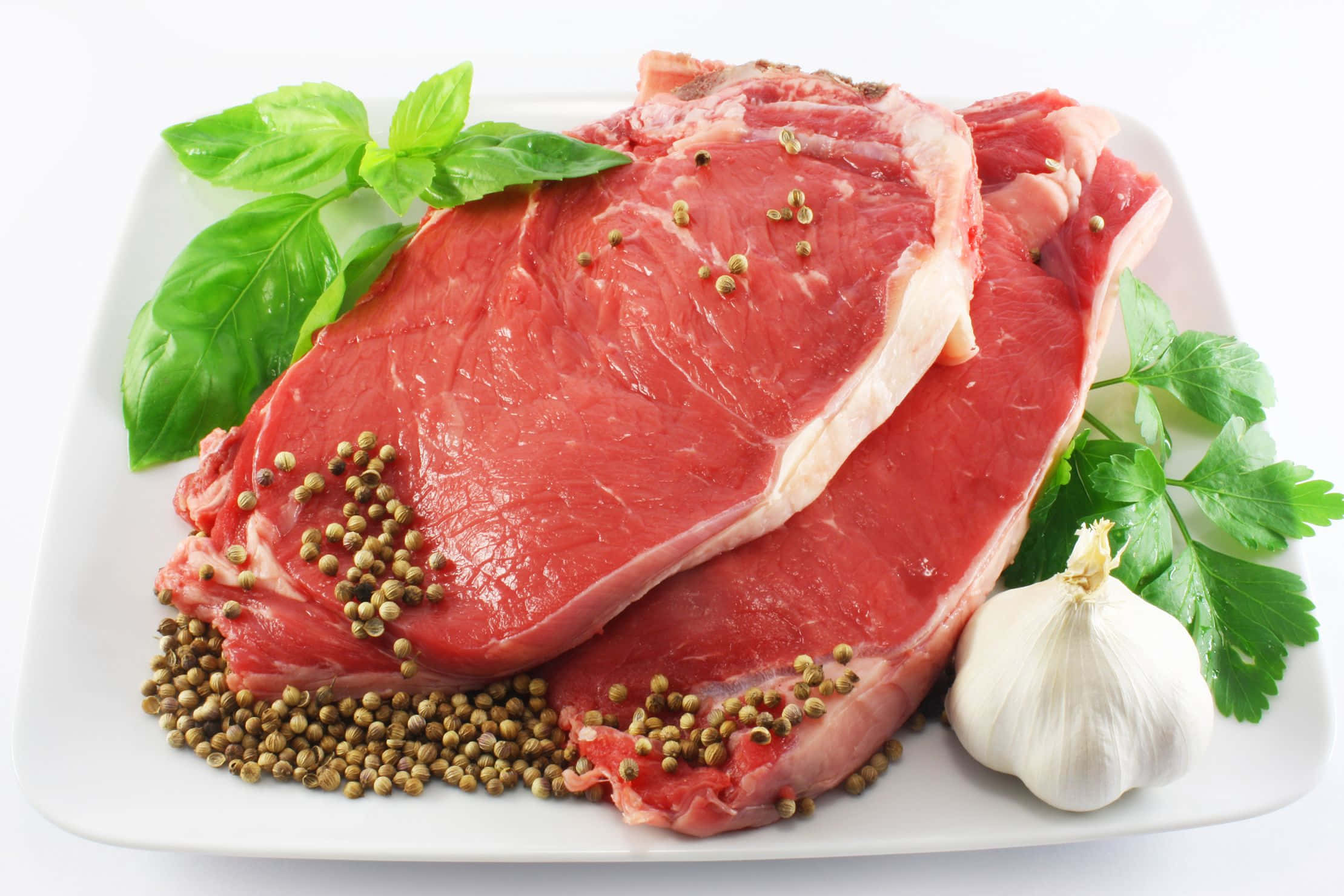 meat 桌布 壁紙 — 兩塊用胡椒粒、羅勒和大蒜調味的生牛肉排放在白色盤子上，背景是潔淨的白色。