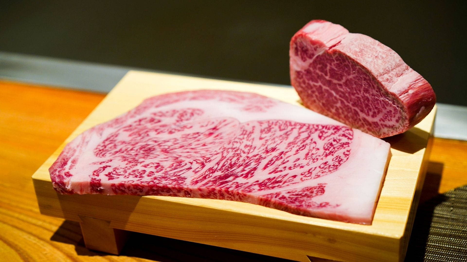 meat 桌布 壁紙 — 兩塊精緻的大理石紋牛肉放在木板上，在溫暖的燈光下展現豐富的紅肉和白色脂肪紋理。