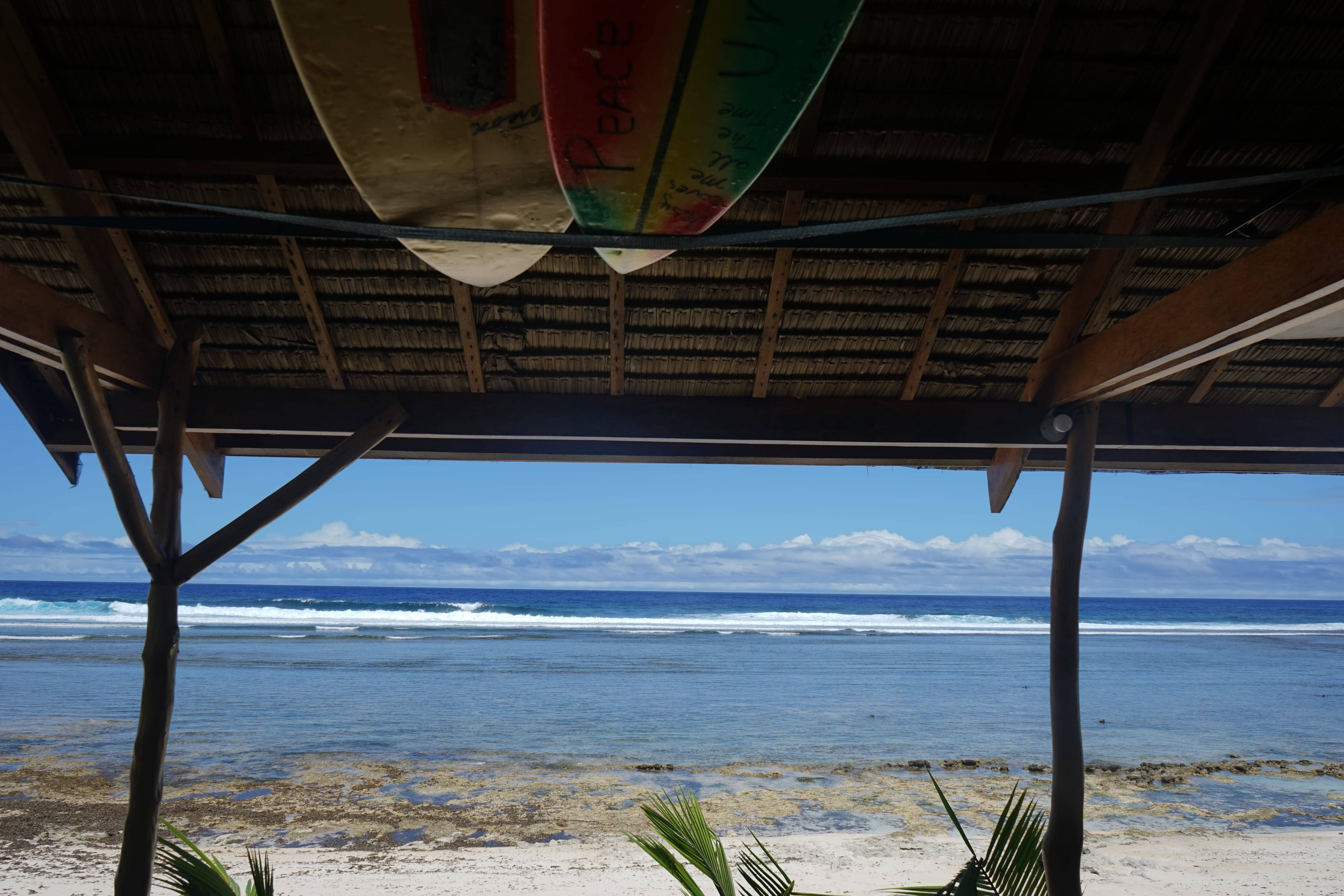 Siargao 桌布 壁紙 — 兩塊衝浪板掛在茅草屋頂下，俯瞰著碧綠的海洋，海浪輕柔，沙灘細軟。