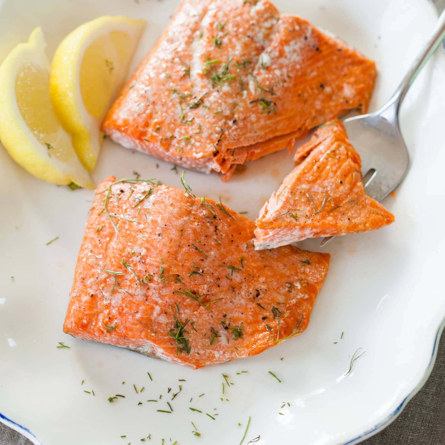 Salmon 桌布 壁紙 — 兩塊調味鮭魚菲力配檸檬角及蒔蘿，放在白色盤子上，附有叉子。