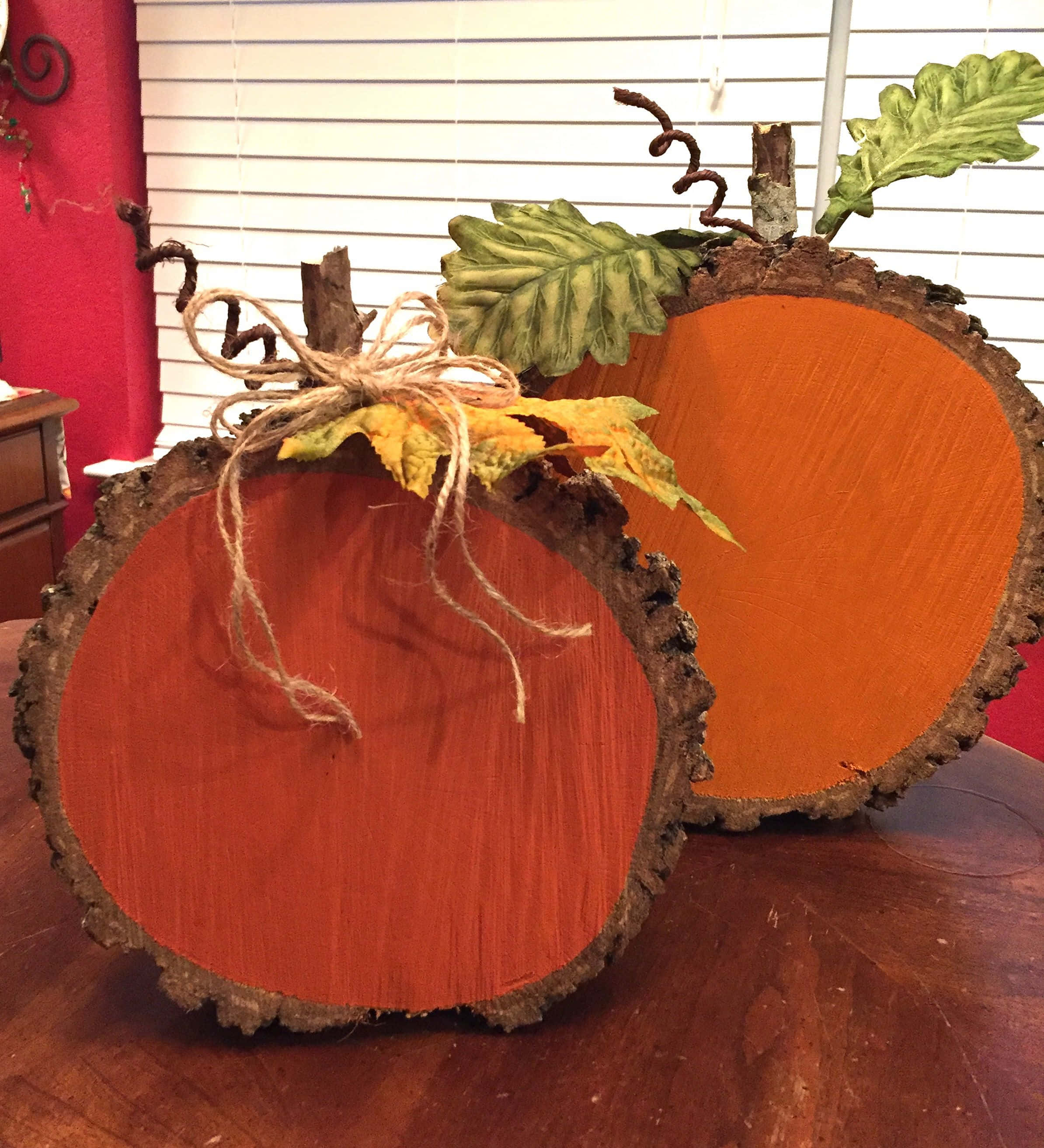 Fall Crafts 桌布 壁紙 — 兩塊質樸的南瓜形木片，塗成橙色，帶有麻繩蝴蝶結和秋葉，放在木桌上。