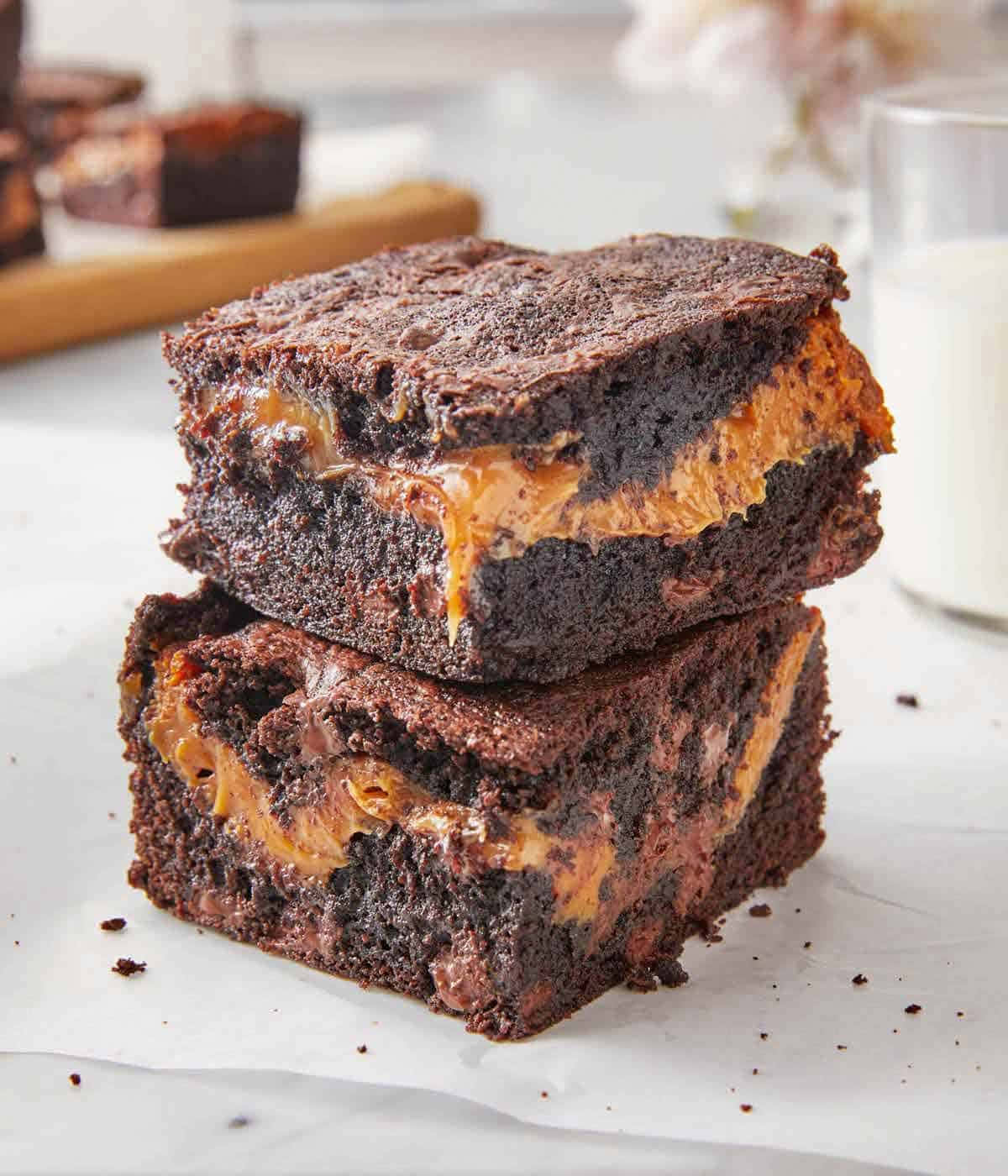 Caramel Brownie 桌布 壁紙 — 兩塊軟心巧克力布朗尼配焦糖漩渦，疊放在烘焙紙上，背景有牛奶。