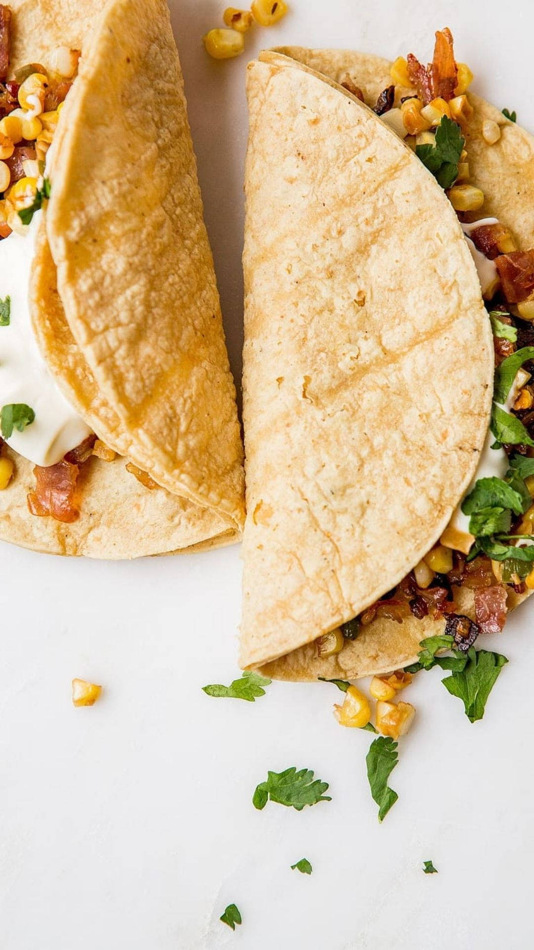 Taco 桌布 壁紙 — 兩塊金黃色玉米餅，餡料豐富，配上新鮮香菜，放在潔白表面上。