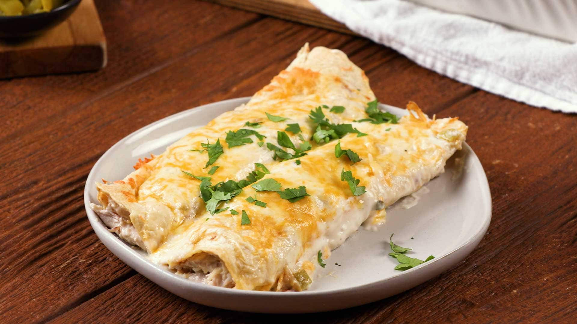 Mexican Food 桌布 壁紙 — 兩塊金黃色的雞肉玉米捲餅，上面覆蓋著融化的起司和新鮮的香菜，放在白色盤子上，置於鄉村風格的木桌上。