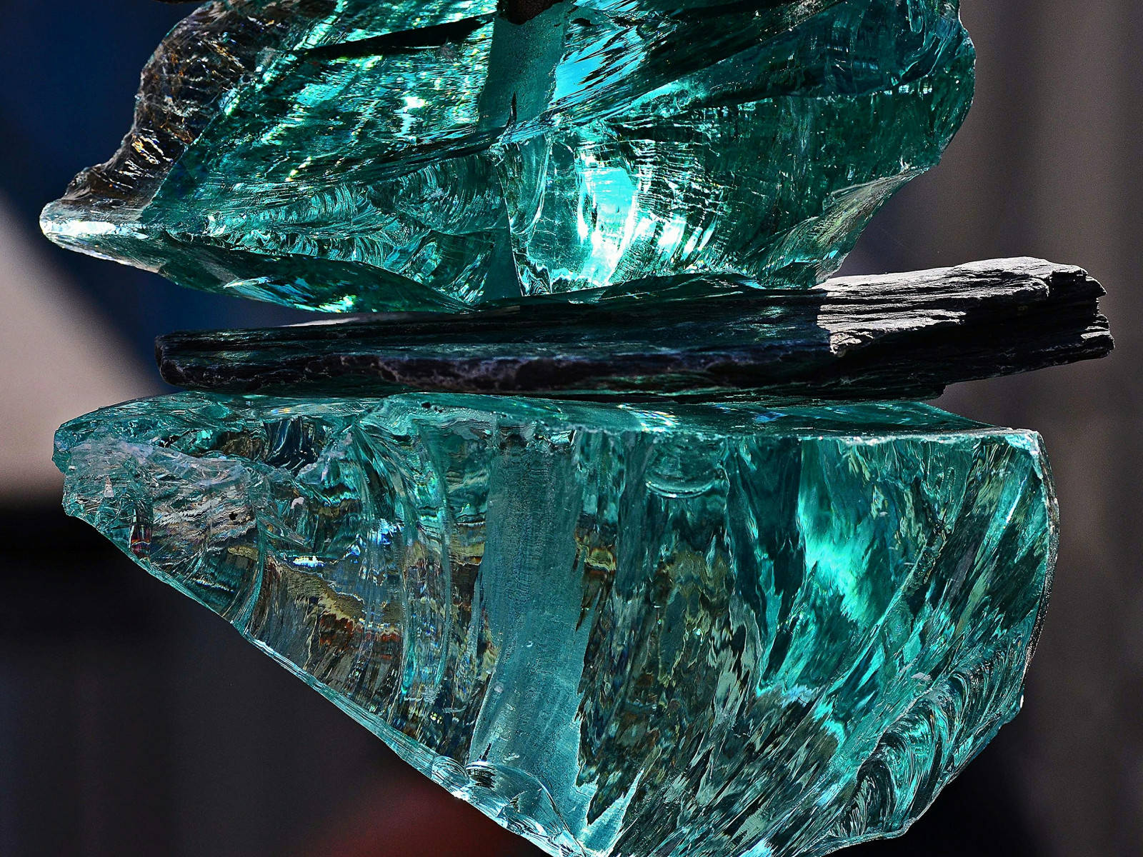 水晶 桌布 壁紙 — 兩塊鋸齒狀的青綠色玻璃碎片在深色石板頂部保持平衡，帶有銳利的反射和深沉的陰影。