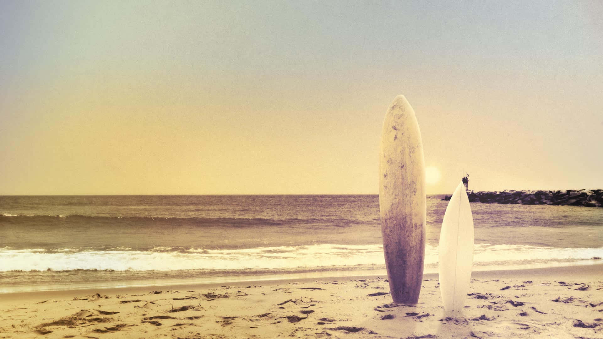 surfing 桌布 壁紙 — 兩塊風化的衝浪板在金色日落時分豎立在沙灘上，溫柔的海浪緩緩湧入。