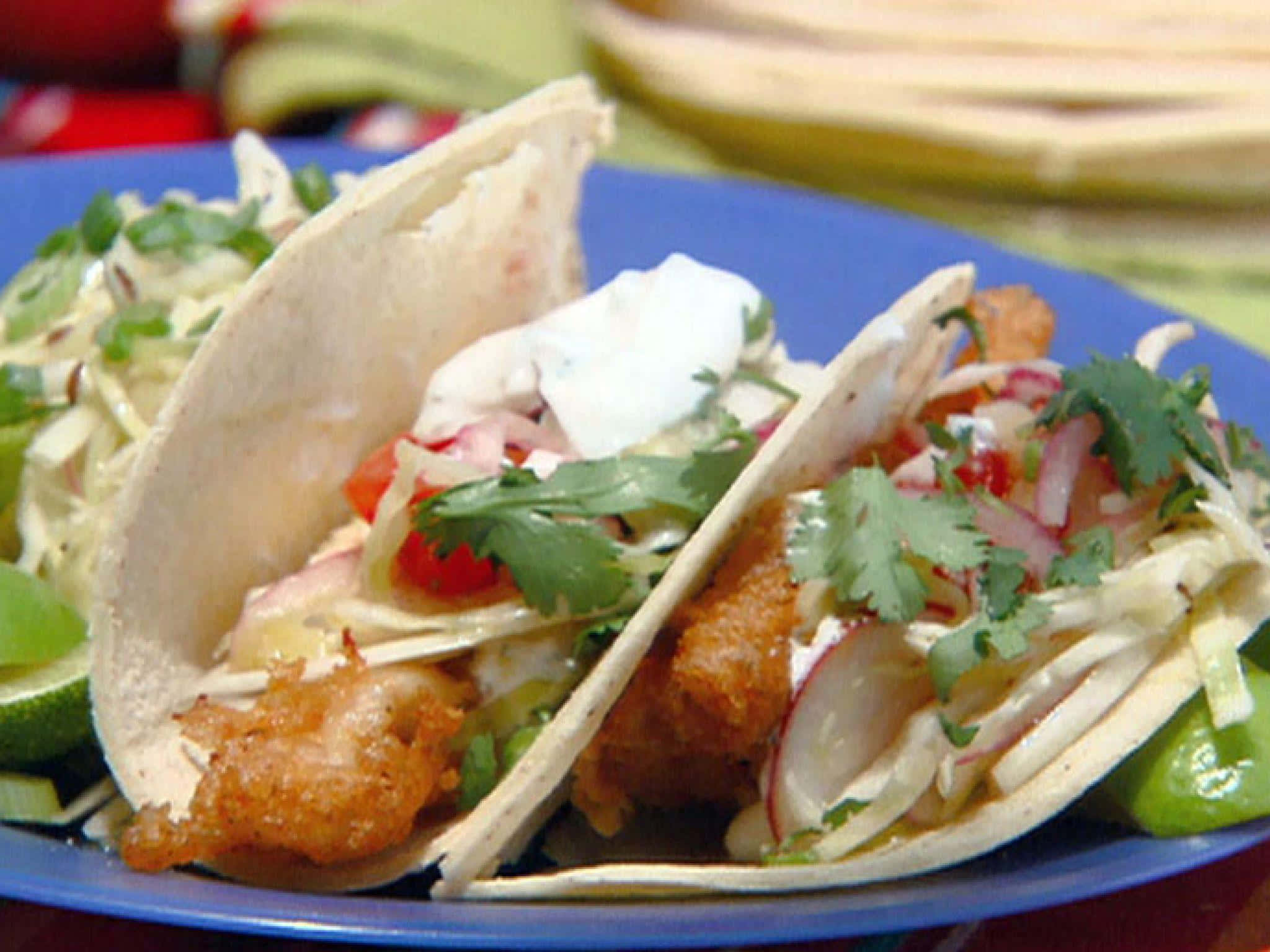 Taco 桌布 壁紙 — 兩塊香脆魚肉墨西哥捲，配上奶油醬、新鮮香菜和蘿蔔片，放在鮮藍色的盤子上。