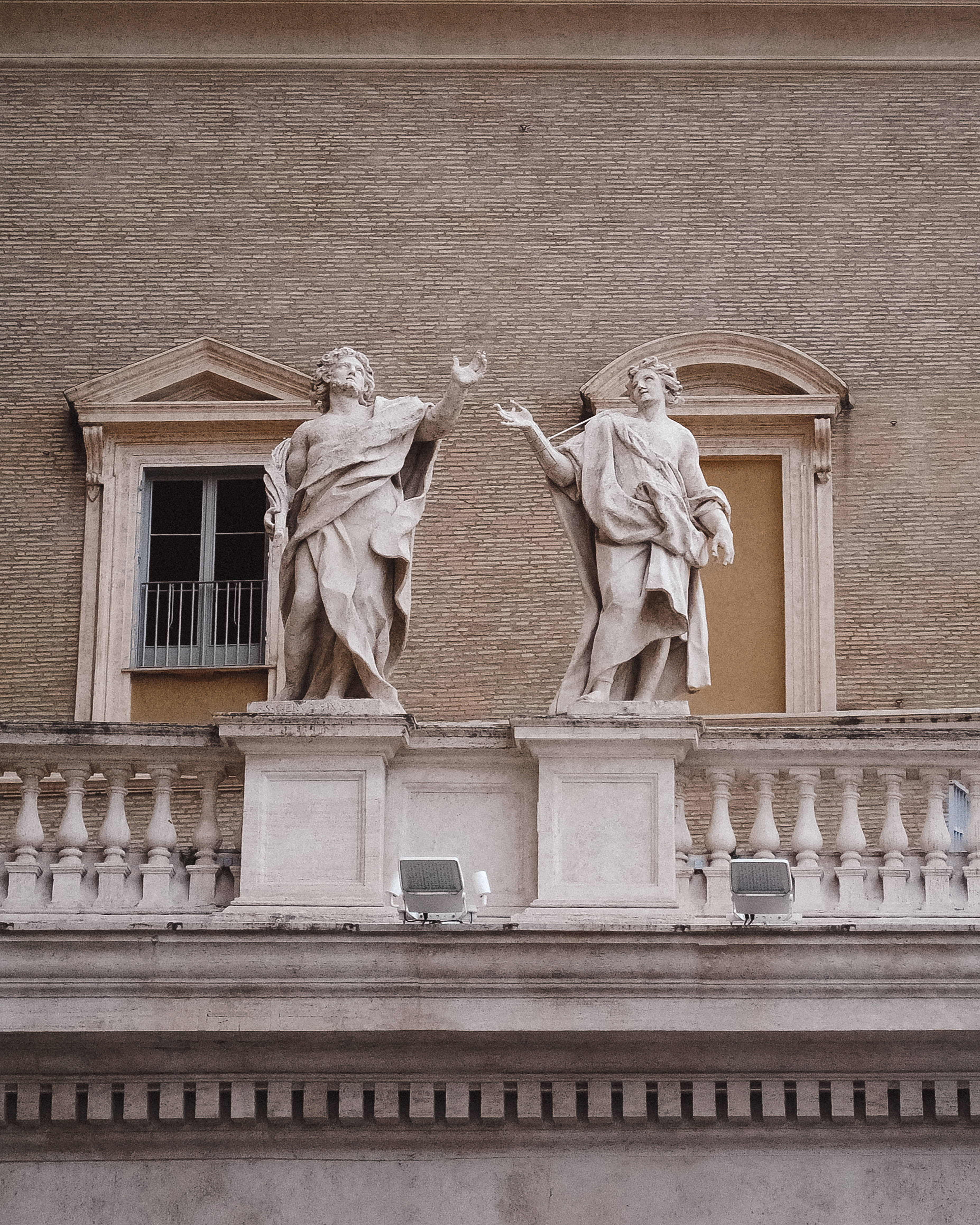 Vatican 桌布 壁紙 — 兩尊穿著長袍的古典石像，在紋理磚砌建築外牆前向上做手勢。