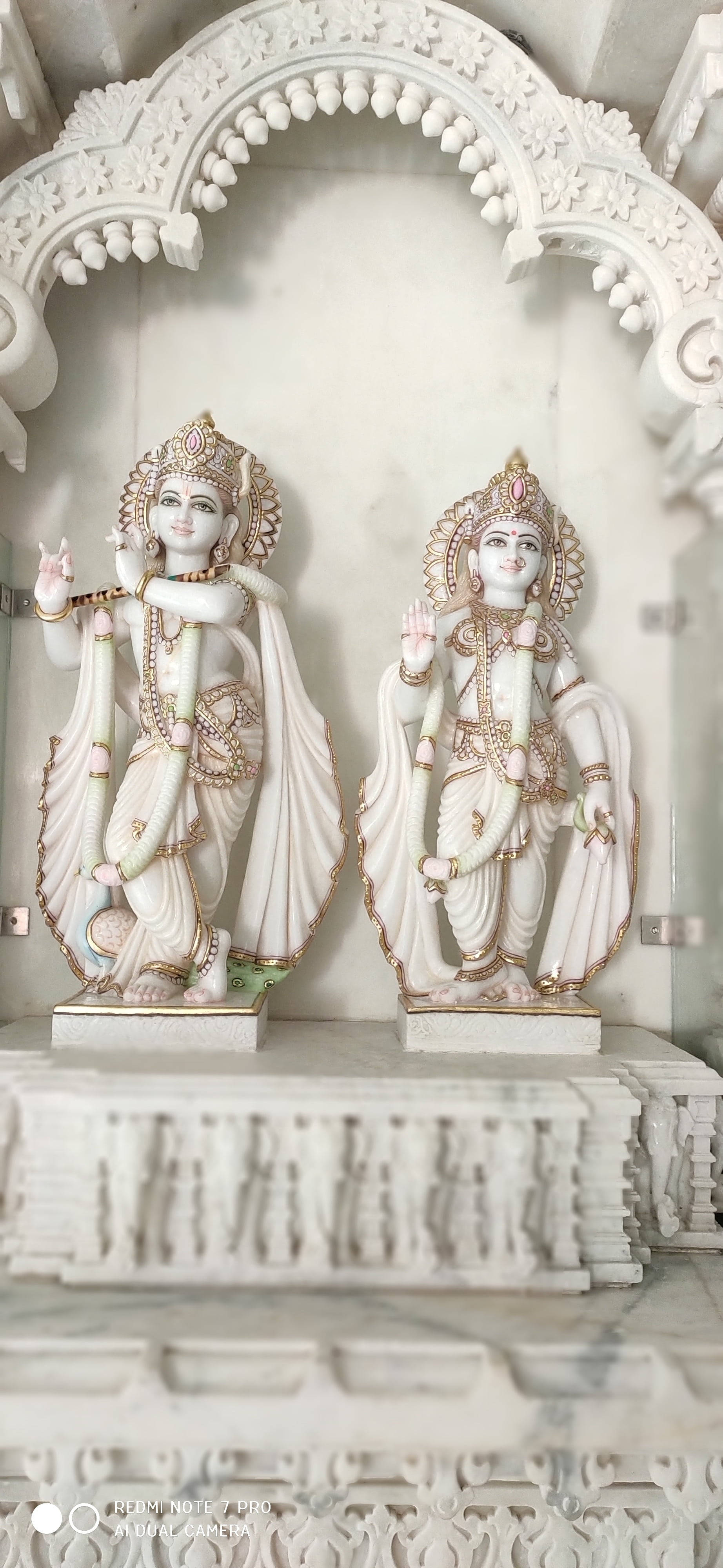krishna iPhone 桌布 壁紙 — 兩尊精雕細琢的白色大理石印度教神像，優雅地立於細節豐富的拱形壁龕下。
