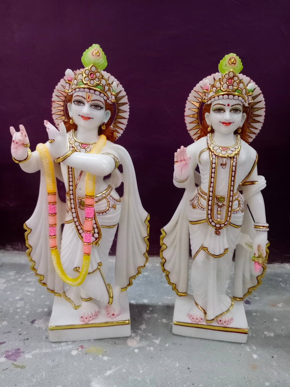 krishna bhagwan 桌布 壁紙 — 兩尊精雕細琢的白色大理石神像，飾有黃金首飾和粉紅色花環，矗立在深紫色背景前。