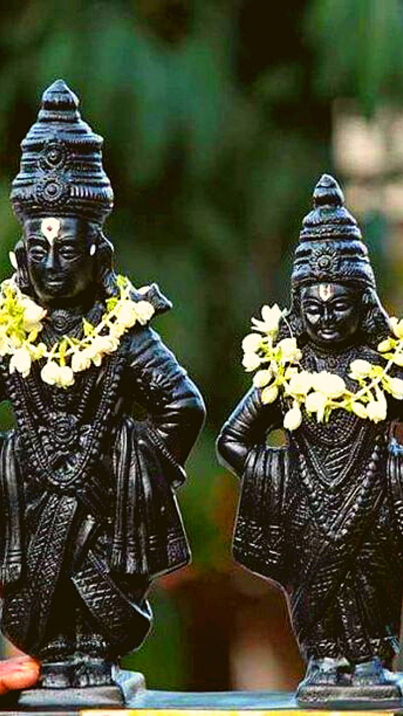 Statue Aesthetic 桌布 壁紙 — 兩尊裝飾華麗的黑色神像，飾有白色花環，並排站在模糊的綠色背景前。