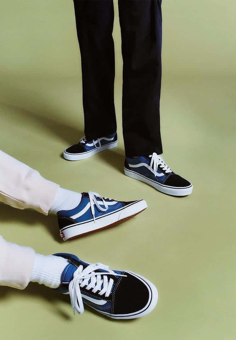 Vans 桌布 壁紙 — 兩對腳穿著黑色和藍色的Vans運動鞋，配白色鞋帶，在柔和的綠色工作室地板上。