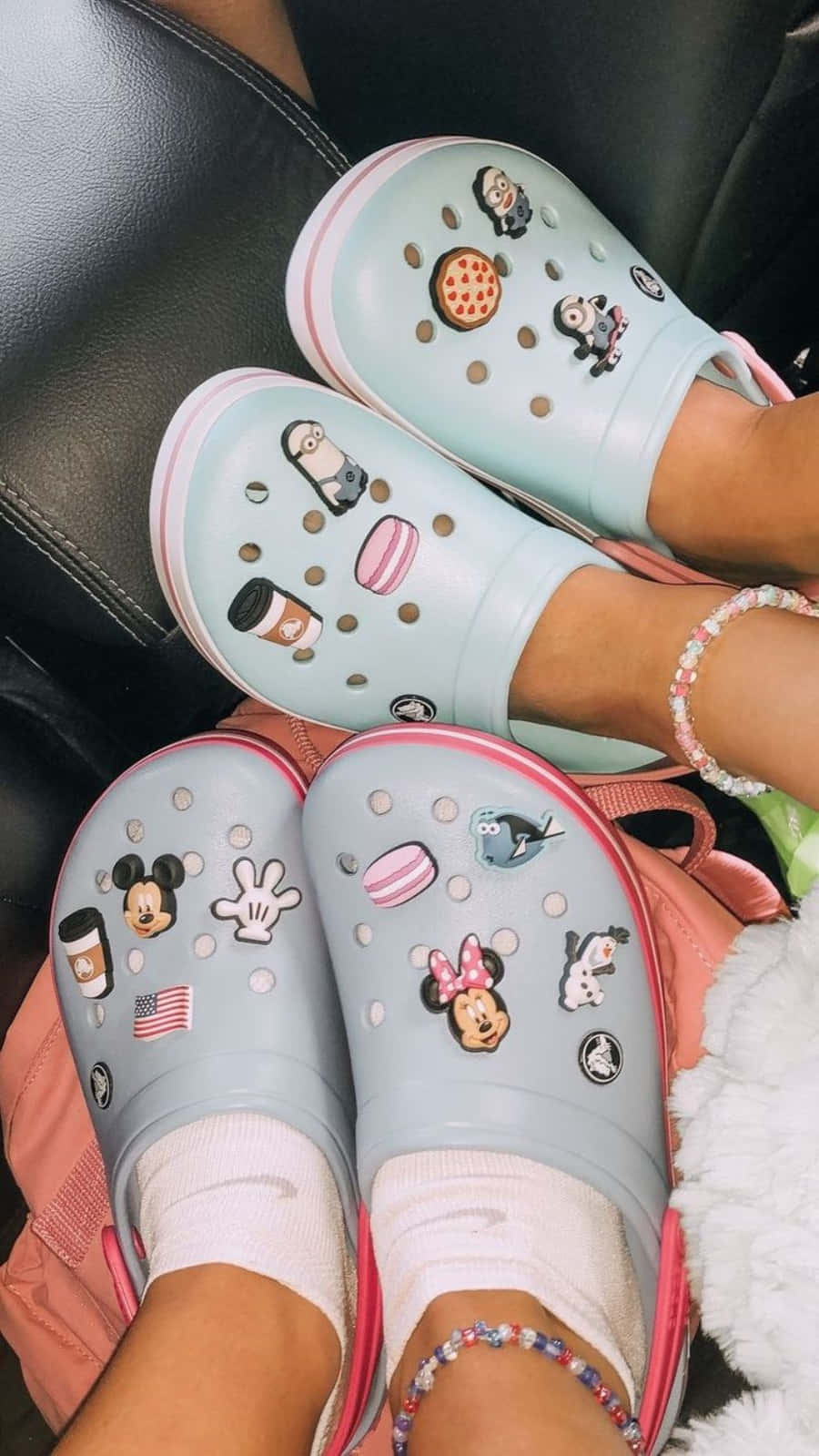 Crocs 桌布 壁紙 — 兩對裝飾過的粉彩Crocs鞋，帶有迪士尼和小小兵吊飾，放在黑色皮沙發上。