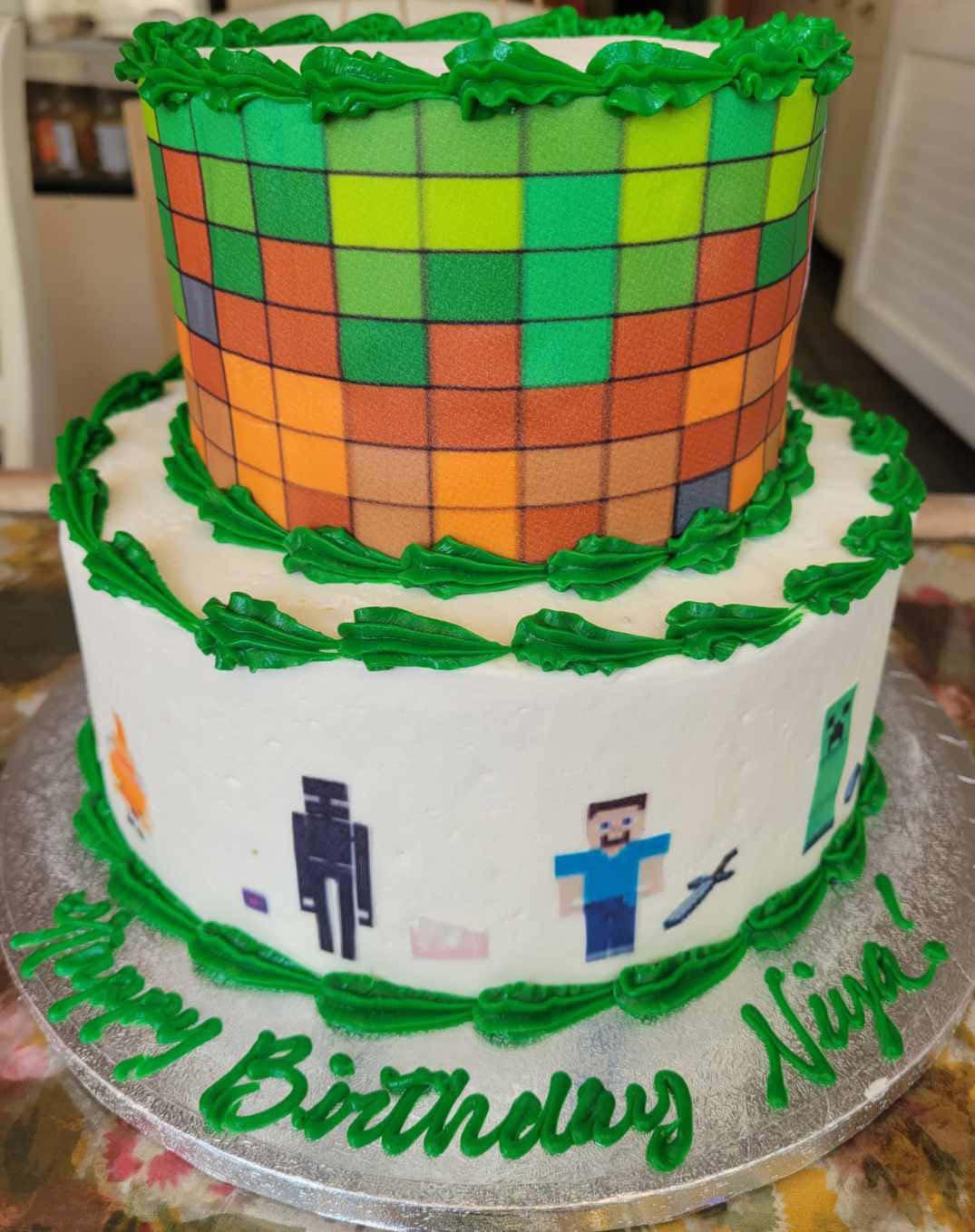 Minecraft Cakes 桌布 壁紙 — 兩層Minecraft主題生日蛋糕，帶有像素化角色和綠色糖霜裝飾。