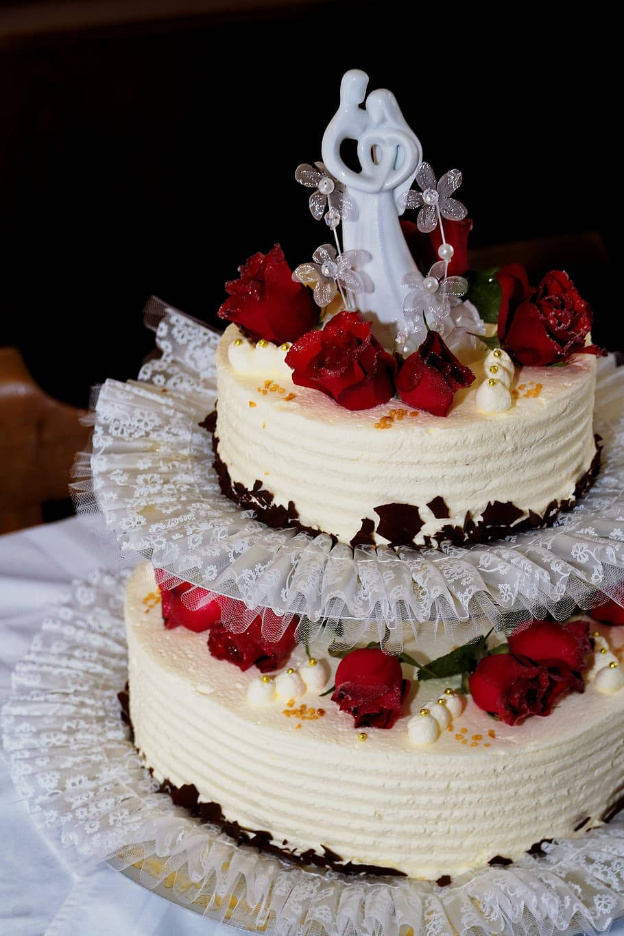 Wedding 桌布 壁紙 — 兩層婚禮蛋糕，飾有紅玫瑰、白色蕾絲和新娘新郎公仔，背景深色。