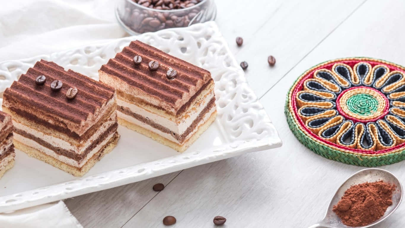 1366x768 Pastries 桌布 壁紙 — 兩層提拉米蘇切片，上面放有咖啡豆，放在白色裝飾盤上，旁邊有一個彩色編織杯墊和一匙可可粉。