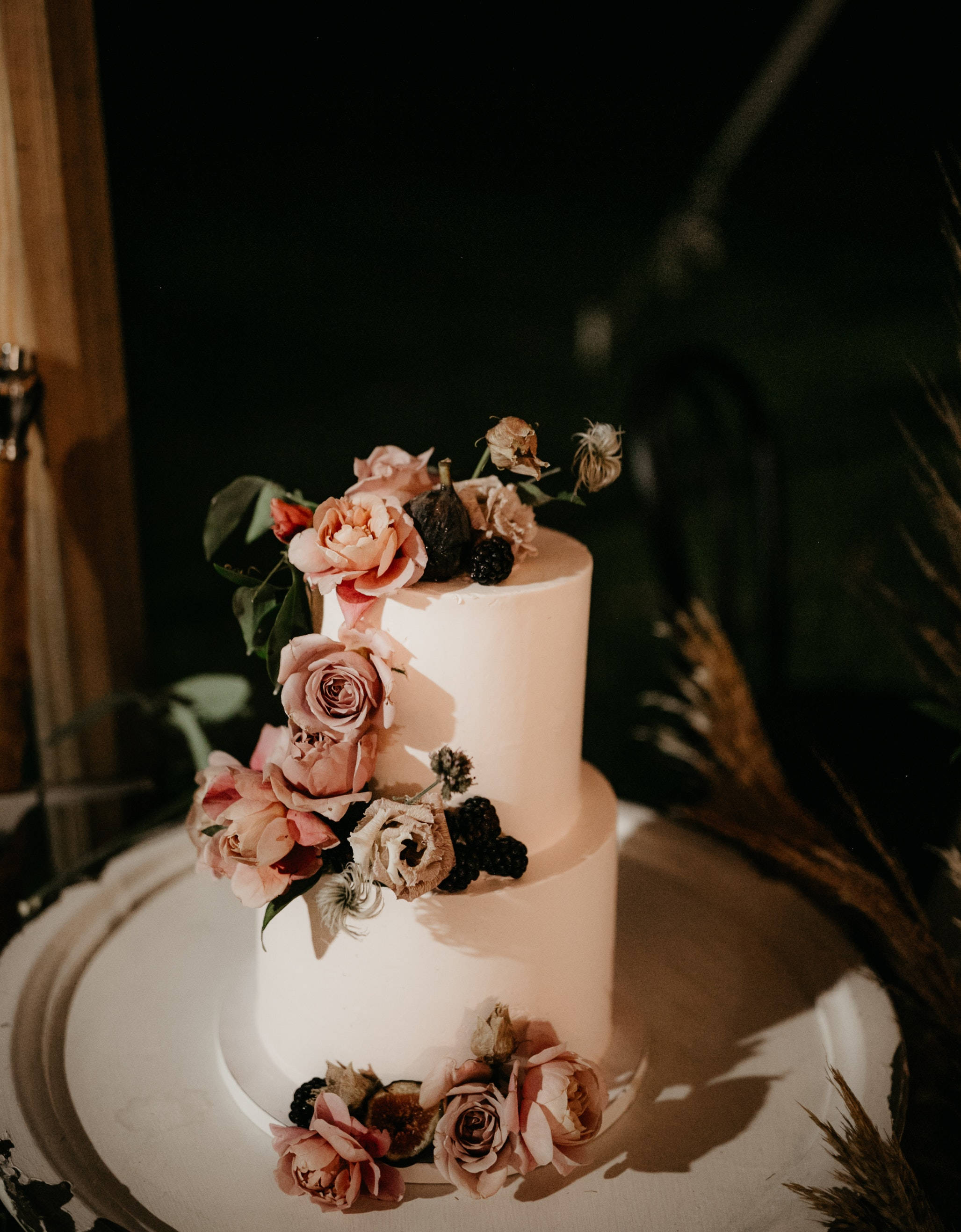 花 桌布 壁紙 — 兩層白色結婚蛋糕，在溫暖的金色燈光下飾以柔和的粉紅玫瑰和黑莓。