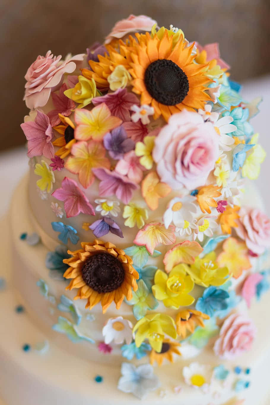 Floral Cake 桌布 壁紙 — 兩層蛋糕，飾以色彩繽紛的糖花，包括向日葵、玫瑰和雛菊，採用柔和粉彩和鮮豔色調。