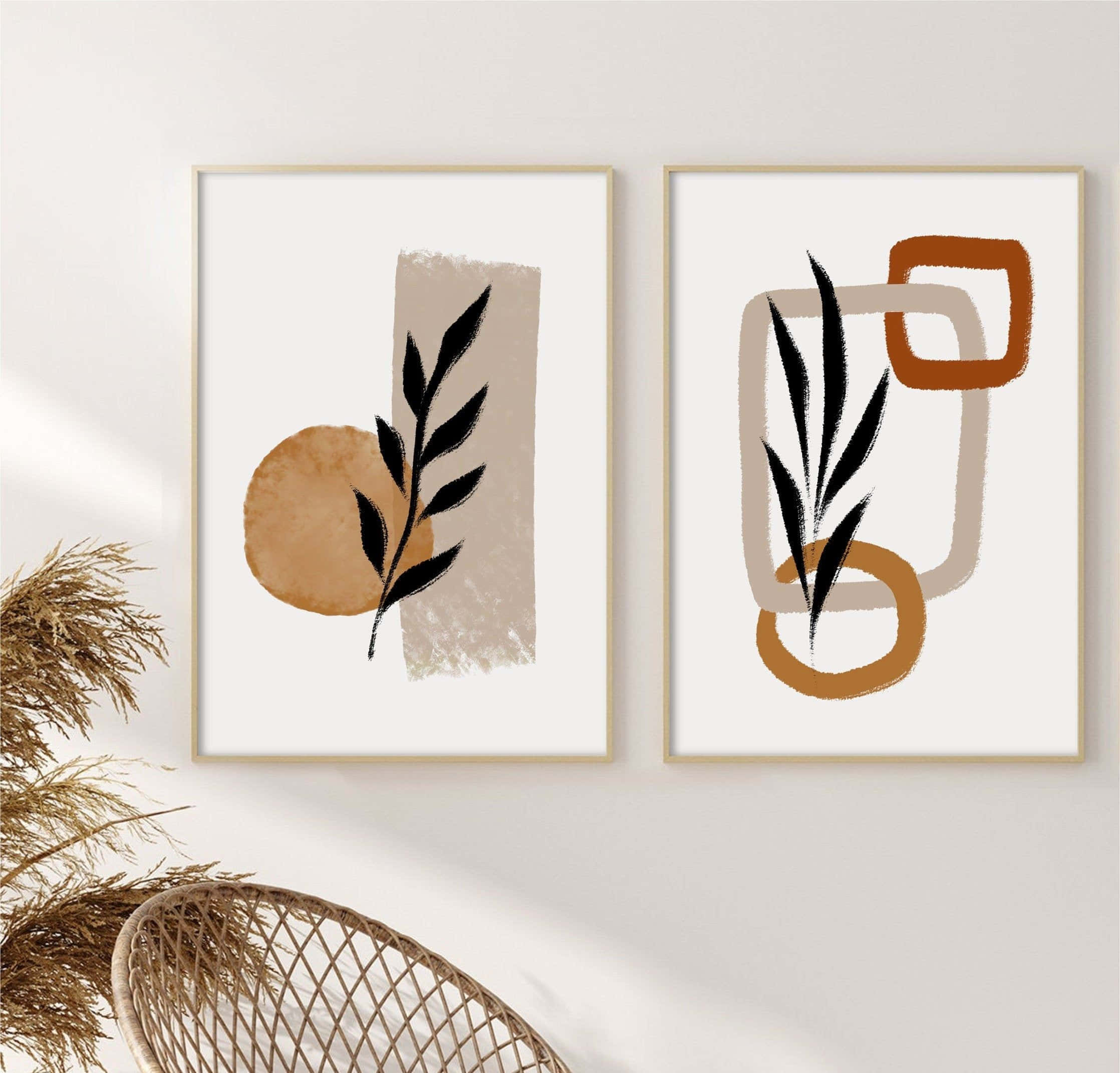Minimalist Painting 桌布 壁紙 — 兩幅極簡風格的抽象裱框藝術品，帶有黑色葉子剪影和大地色幾何形狀，掛在白色牆上，旁邊有一張編織椅和乾草。