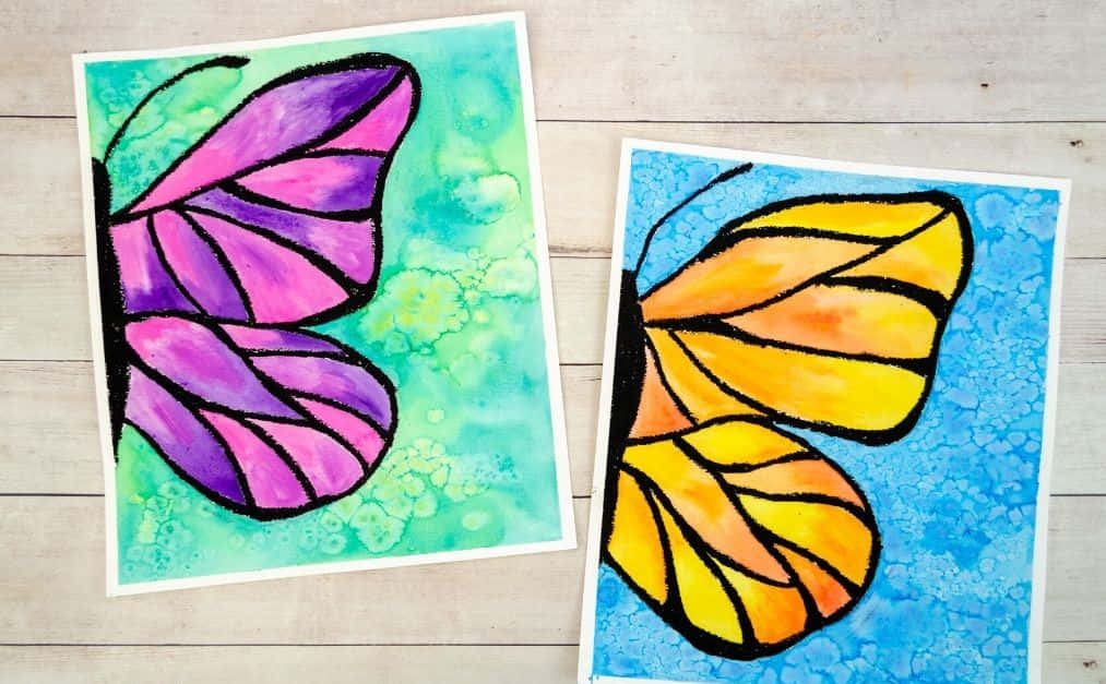 Beautiful Art 桌布 壁紙 — 兩幅色彩鮮豔的蝴蝶畫作，帶有紫色和黃色的翅膀，放在有紋理的背景上，擱在淺色木質表面上。
