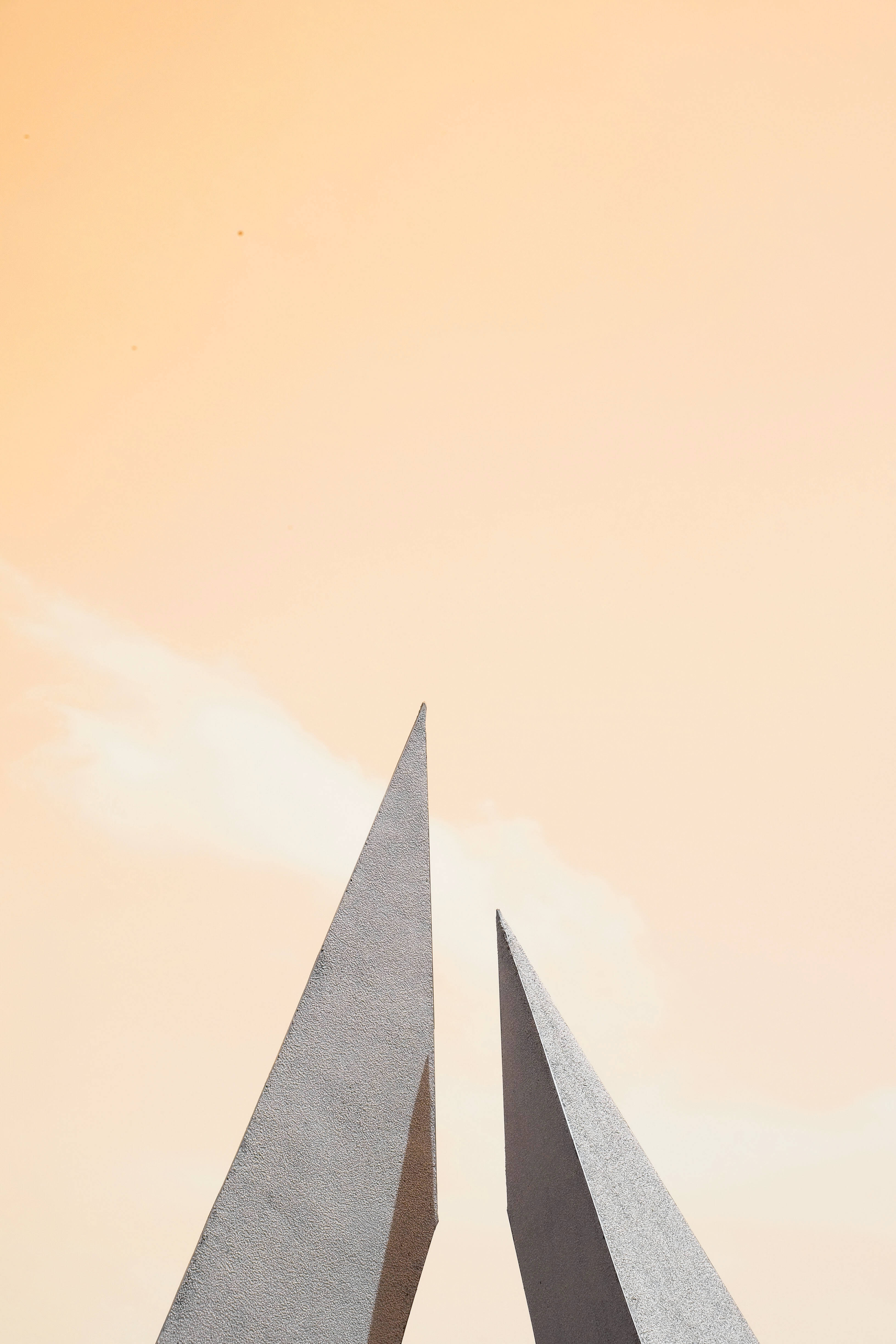 Cute Pastel Aesthetic 桌布 壁紙 — 兩座尖銳的混凝土尖塔刺穿柔和的桃色天空，伴隨著縷縷薄雲，正值黃金時刻。