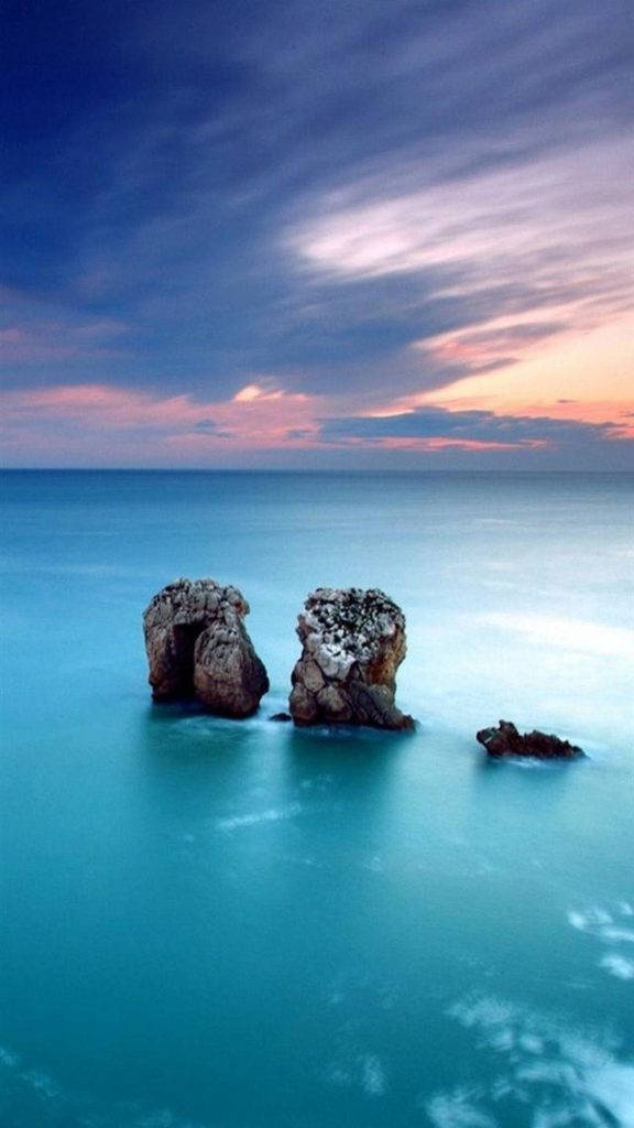 X 桌布 壁紙 — 兩座崎嶇的海蝕柱在平靜的碧綠海水中高聳，上方是佈滿粉紅和紫色雲彩的戲劇性暮色天空。