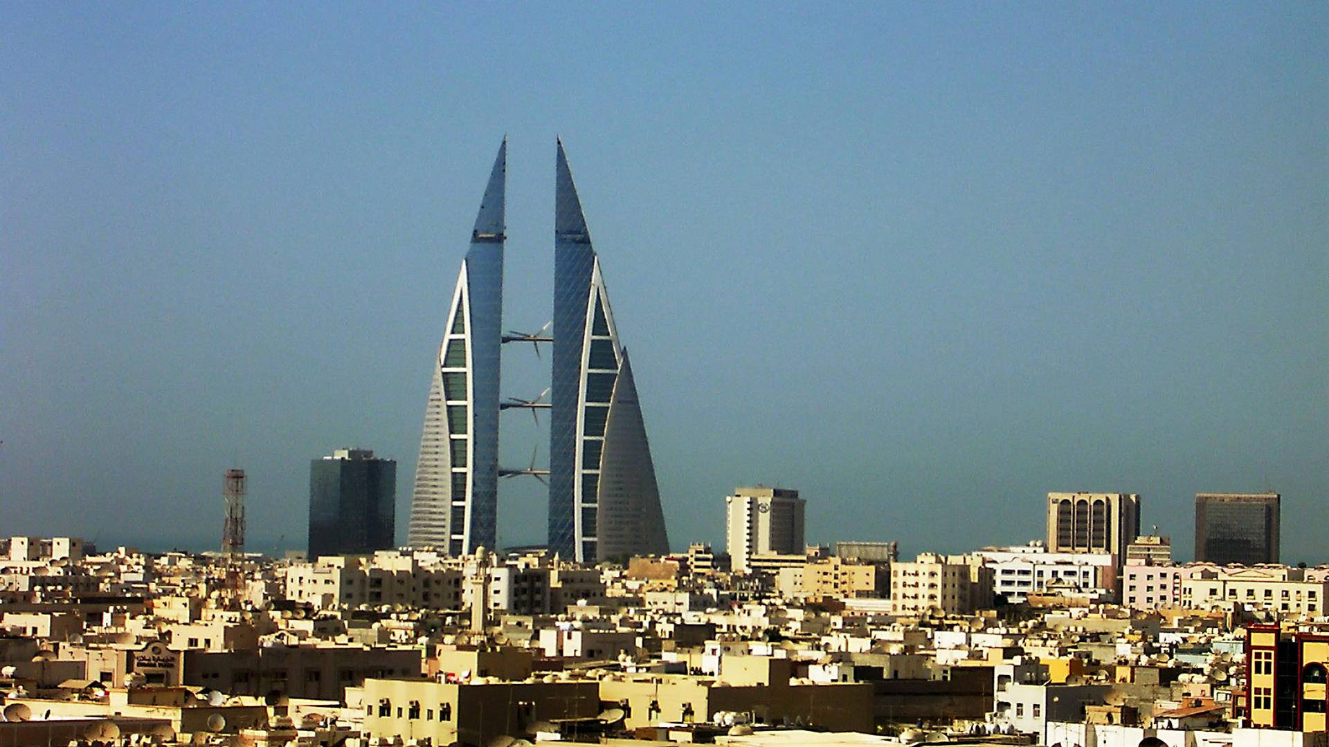 Bahrain 桌布 壁紙 — 兩座標誌性的帆形摩天大樓在晴朗的藍天下聳立於密集的城市天際線之上。