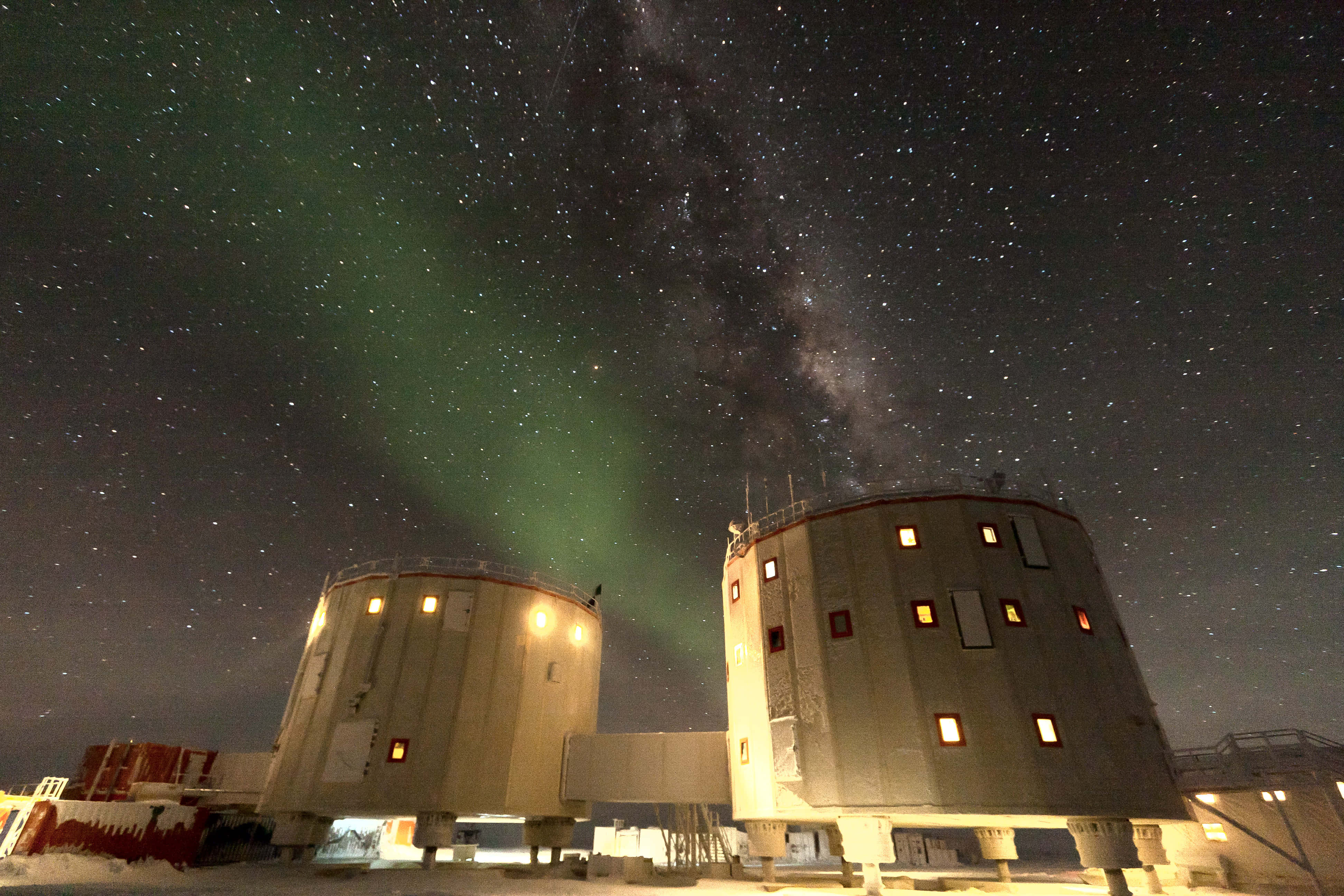 Antarctica 桌布 壁紙 — 兩座發光的圓柱形建築矗立在星空下，上方有鮮豔的綠色北極光拱起。
