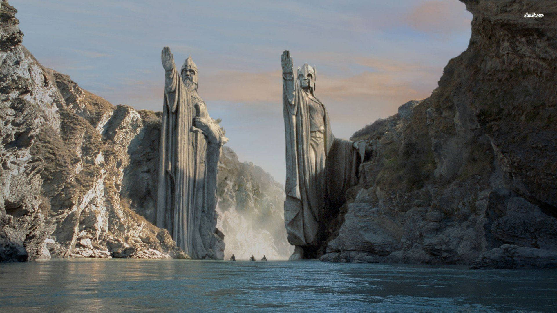 Lotr 桌布 壁紙 — 兩座穿著長袍的巨大石像矗立在峽谷中，旁邊有一條河流，河上有小船漂流。