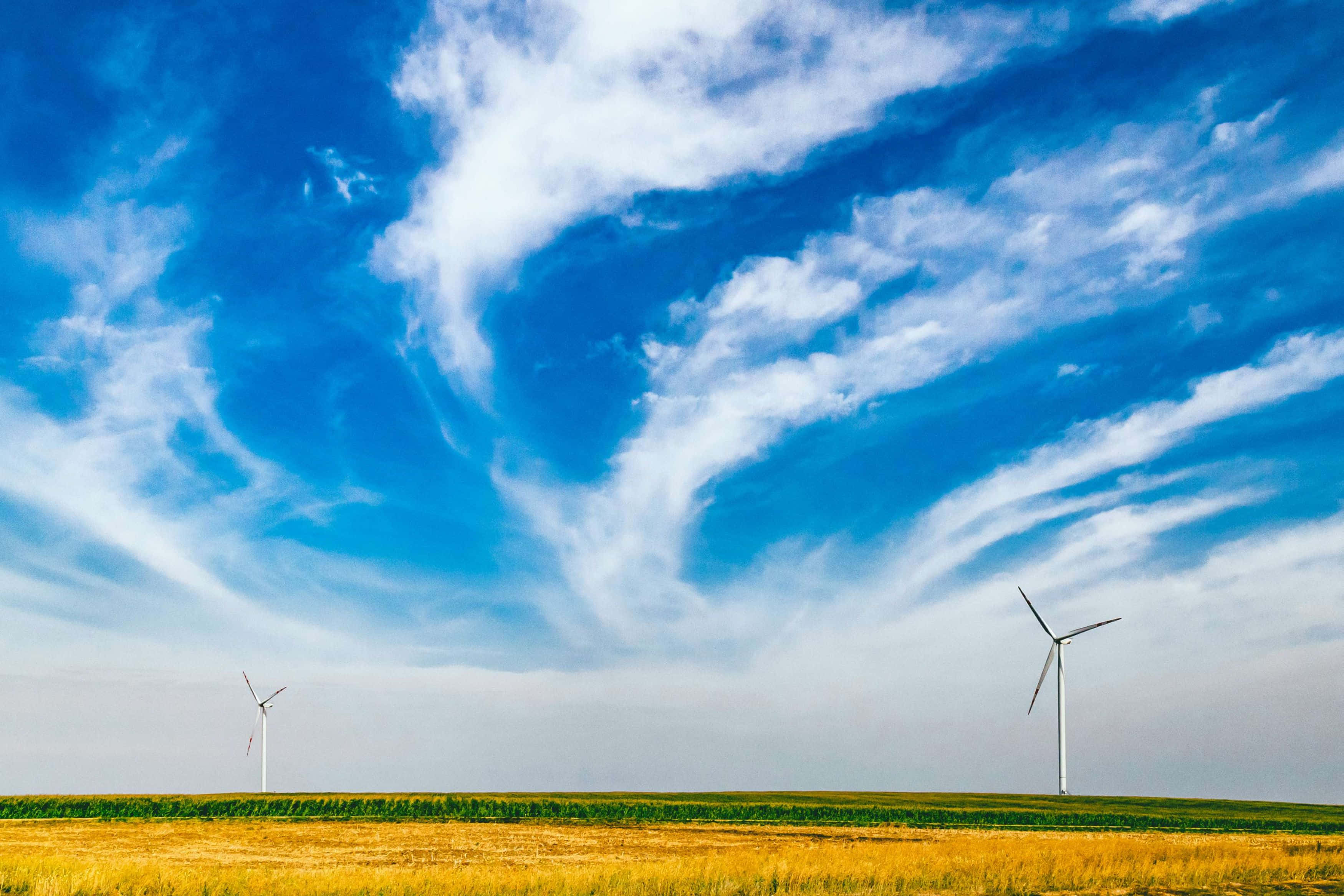 Renewable Energy 桌布 壁紙 — 兩座風力發電機高聳在金黃色的田野上，背景是廣闊的藍天，點綴著縷縷白雲。