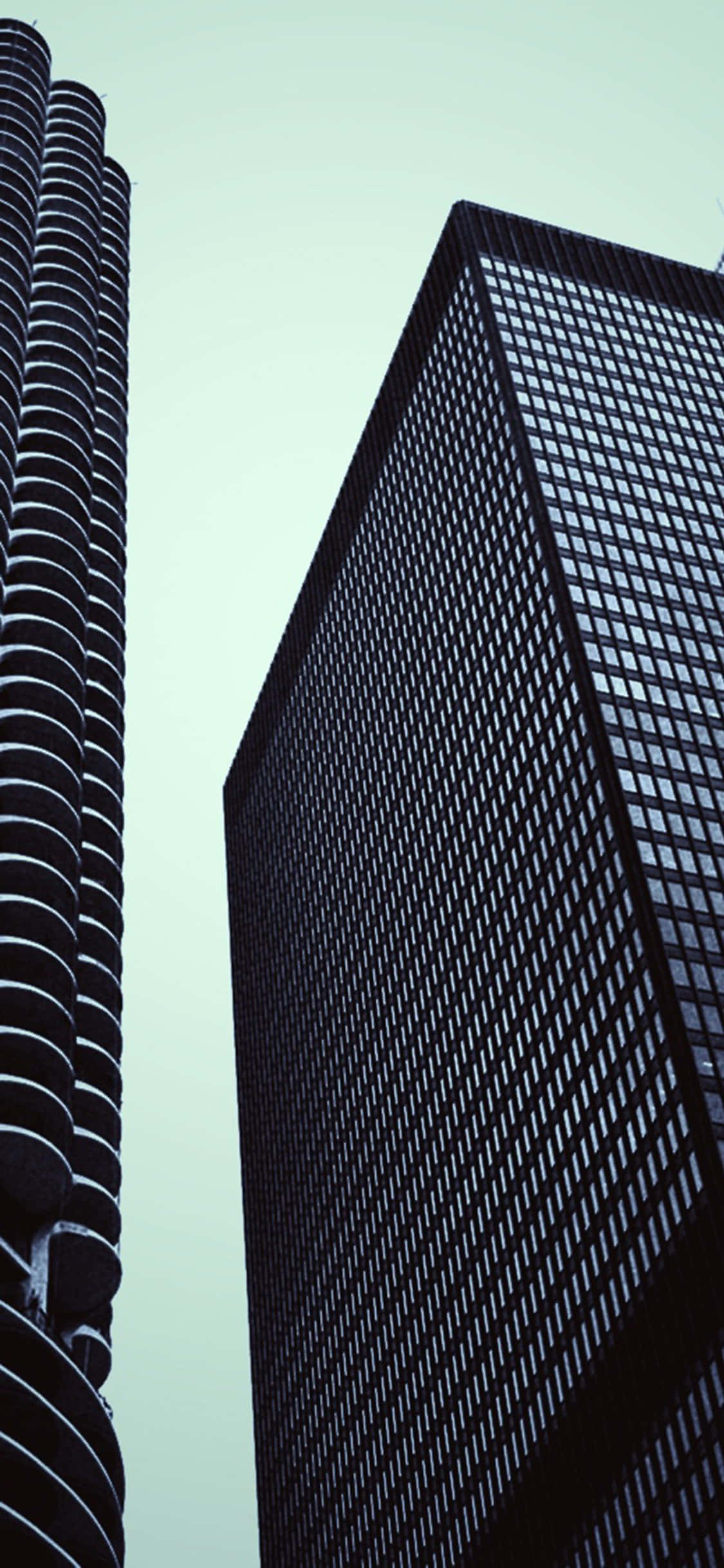 Modernism 桌布 壁紙 — 兩座高聳的摩天大樓在蒼白的天空下矗立，一座有弧形陽台，另一座有網格狀窗戶。