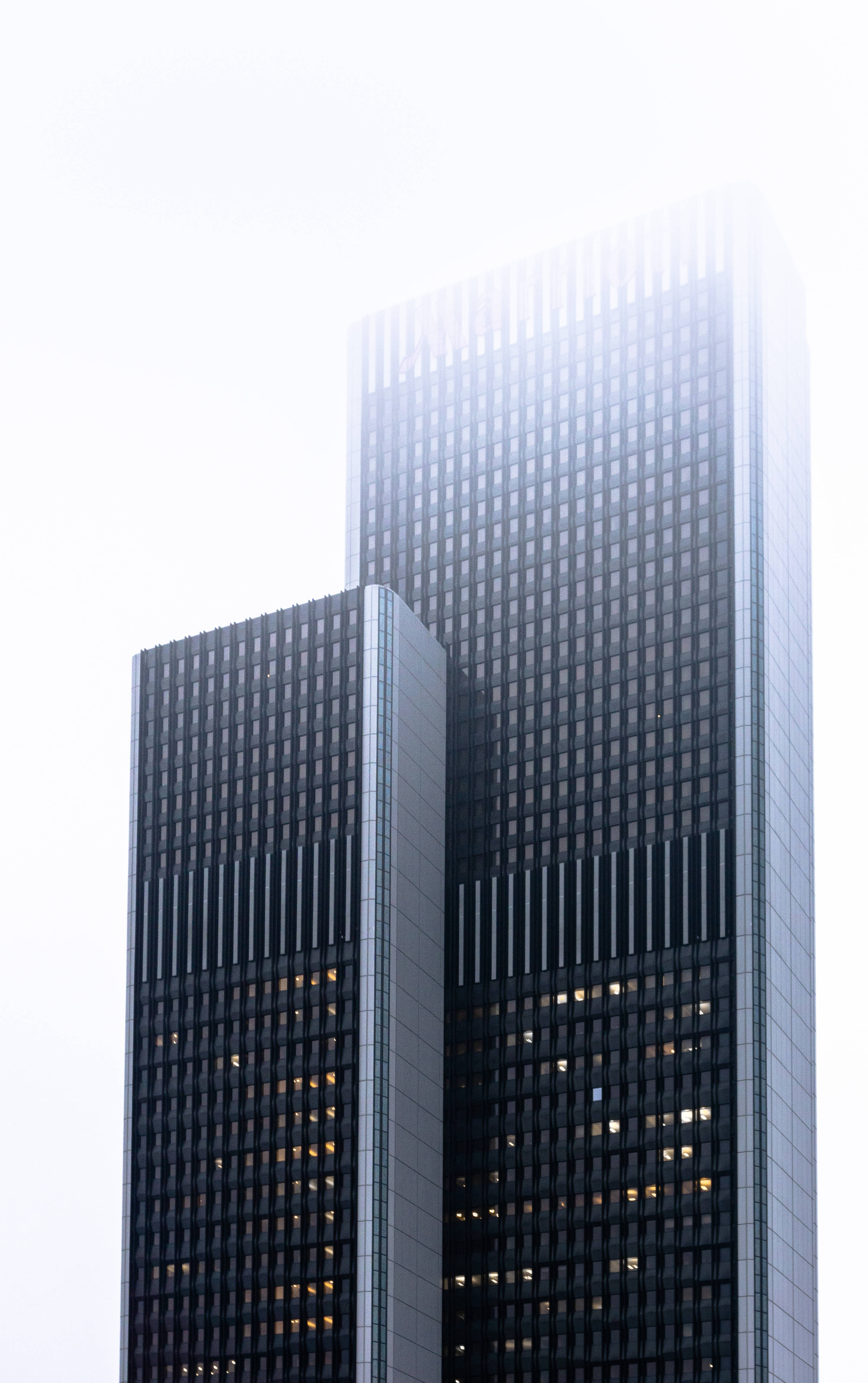 Skyscraper 桌布 壁紙 — 兩座高聳的玻璃摩天大樓刺穿朦朧的天空，亮著的窗戶在霧氣繚繞的背景中閃耀。