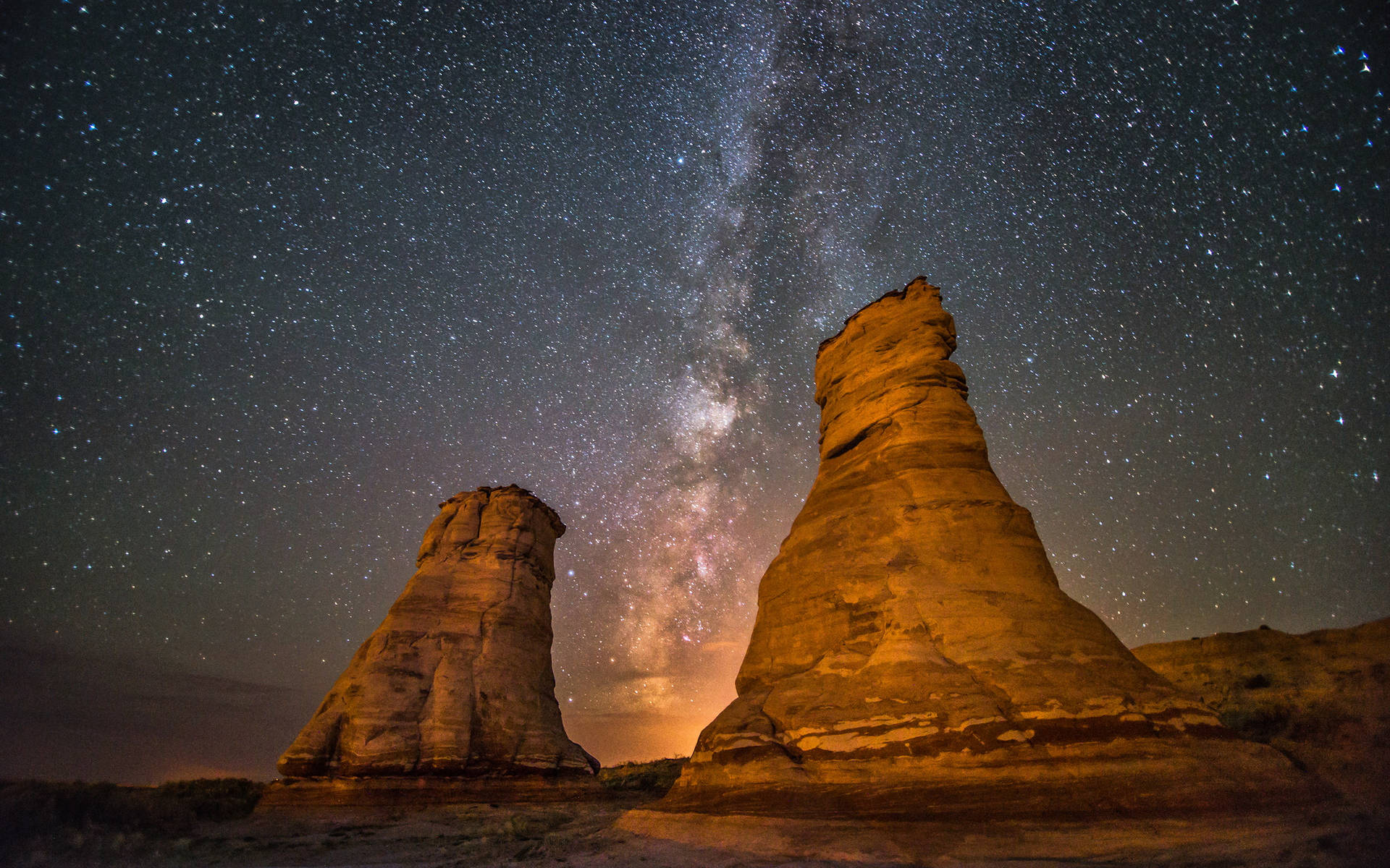 在繁星點點的夜空下，兩座被照亮的岩石地貌，銀河清晰可見。