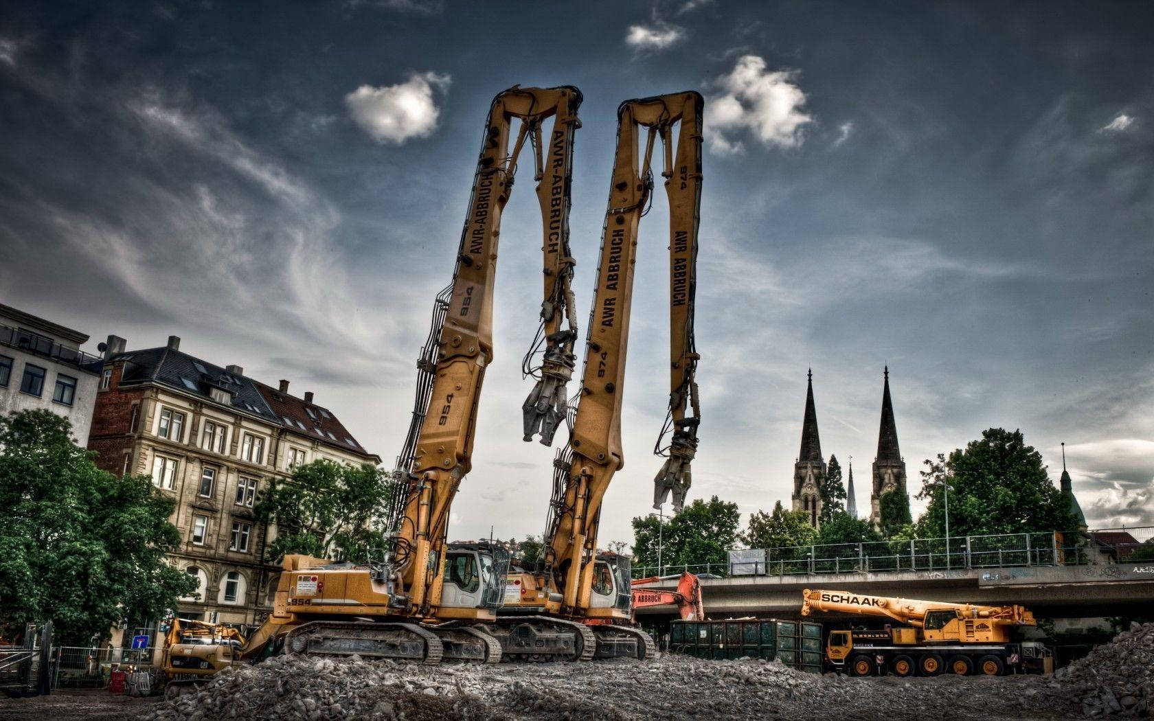 construction 桌布 壁紙 — 兩座高聳的黃色挖掘機矗立在瓦礫中，背景是戲劇性的多雲天空和歷史尖塔。