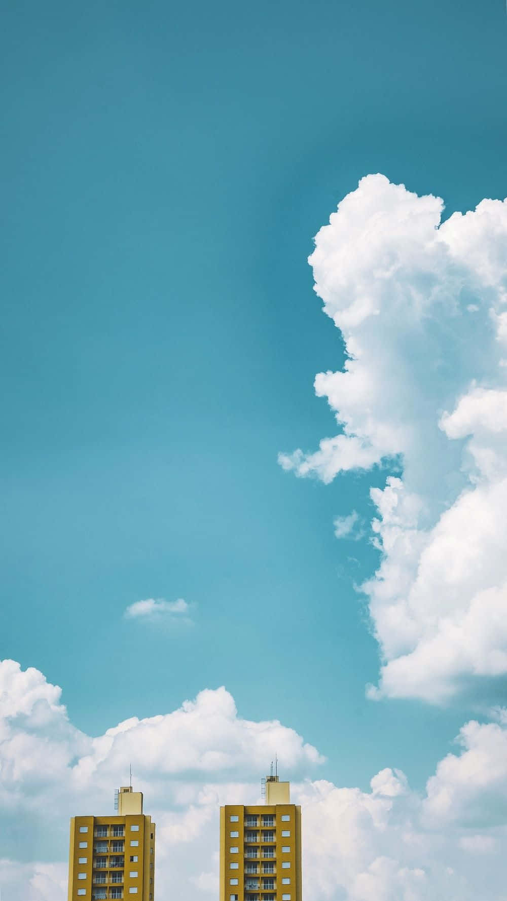Beautiful Sky 桌布 壁紙 — 兩座黃色公寓大樓在廣闊的藍綠色天空中聳立，天空佈滿蓬鬆的白雲。