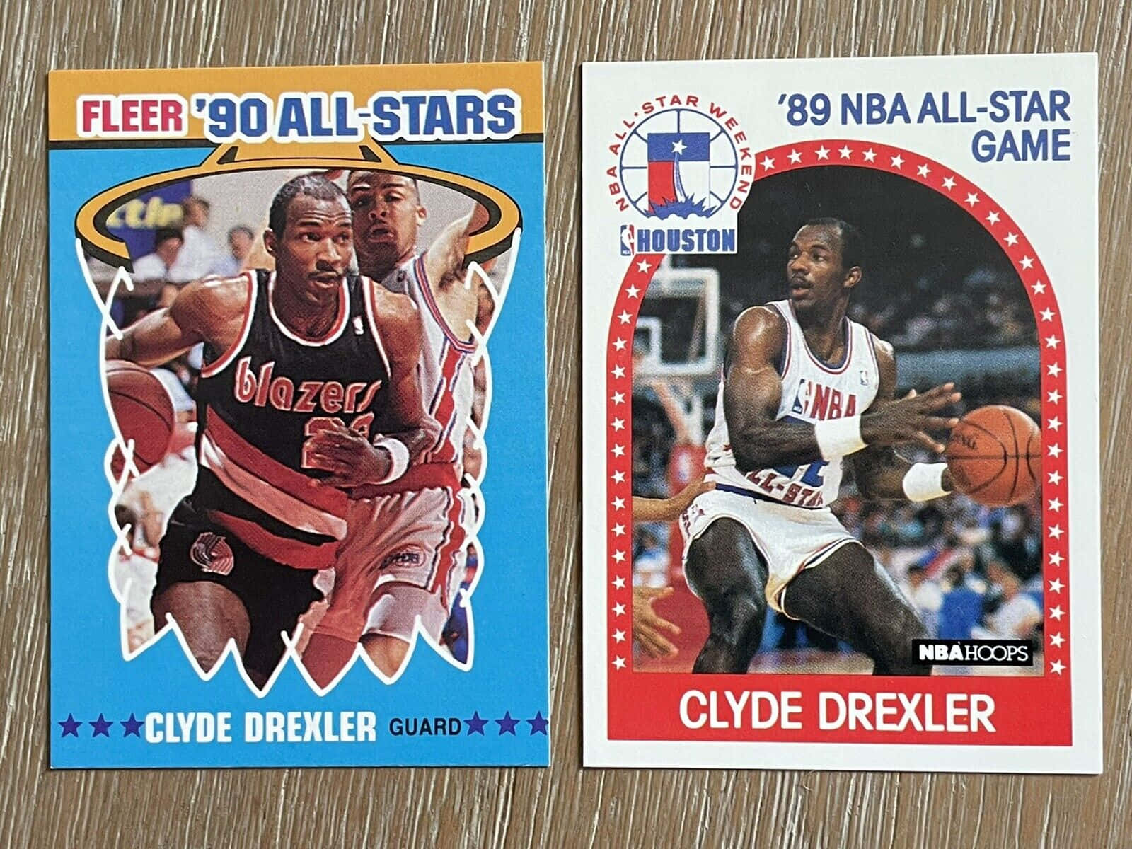 兩張 1980 年代 Clyde Drexler 的 NBA 全明星交換卡在木頭上。 — NBA 壁紙
