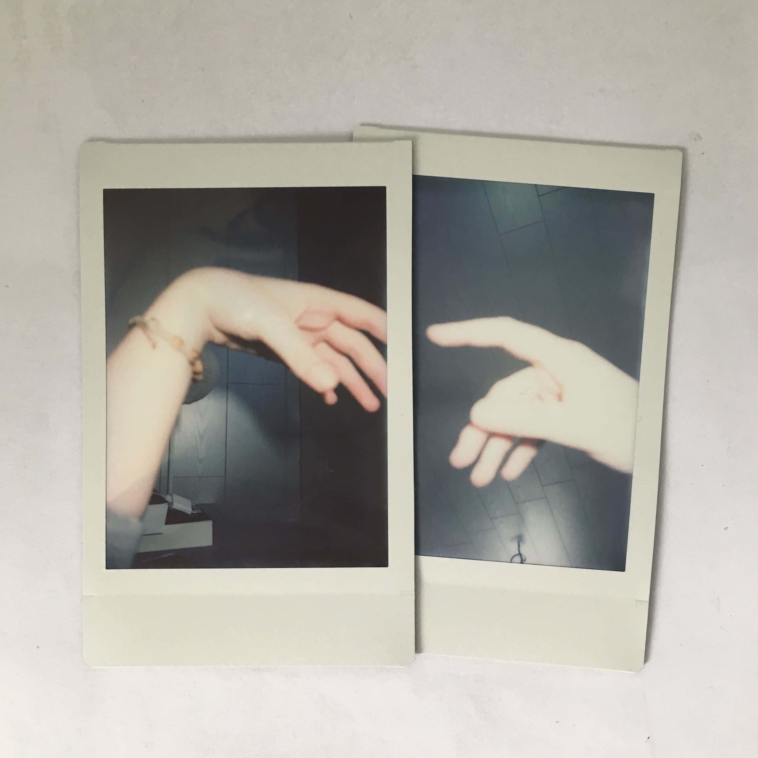 Aesthetic Polaroid 桌布 壁紙 — 兩張拍立得照片顯示在昏暗燈光下的手，一隻戴著手鐲，另一隻指向瓷磚地板。