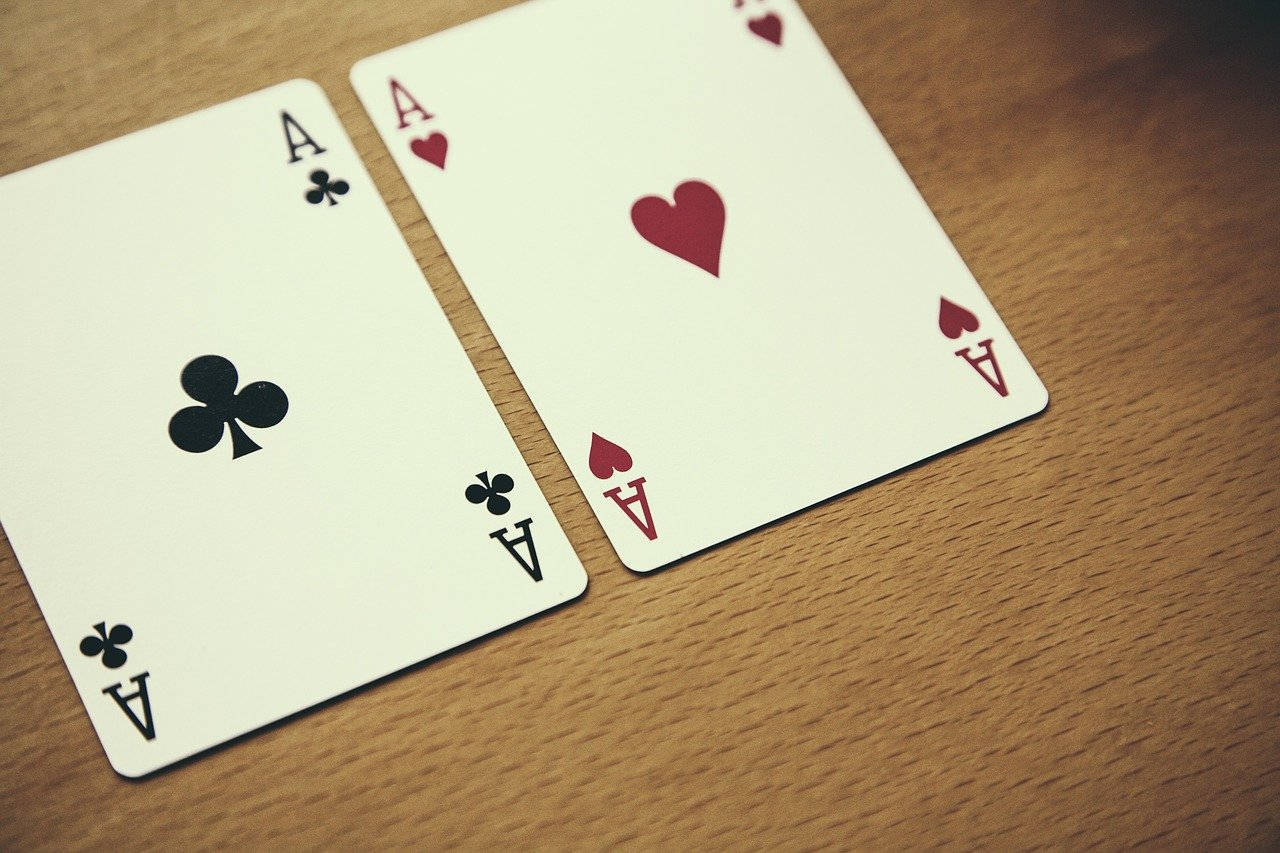 Playing Cards 桌布 壁紙 — 兩張撲克牌，梅花A和紅心A，放在溫暖的木質表面上，帶有柔和自然光。