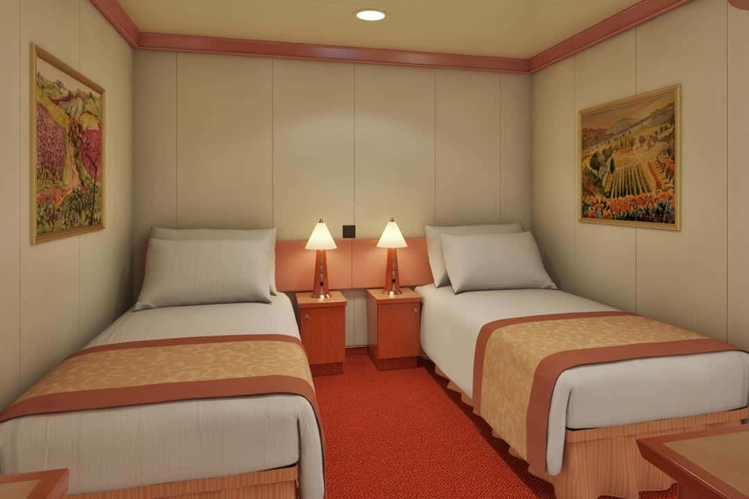 Carnival Conquest 桌布 壁紙 — 兩張整齊鋪好的床，帶有橙色點綴和溫暖的燈光，在舖有紅色地毯和掛有框畫葡萄園藝術品的舒適小木屋中閃耀。