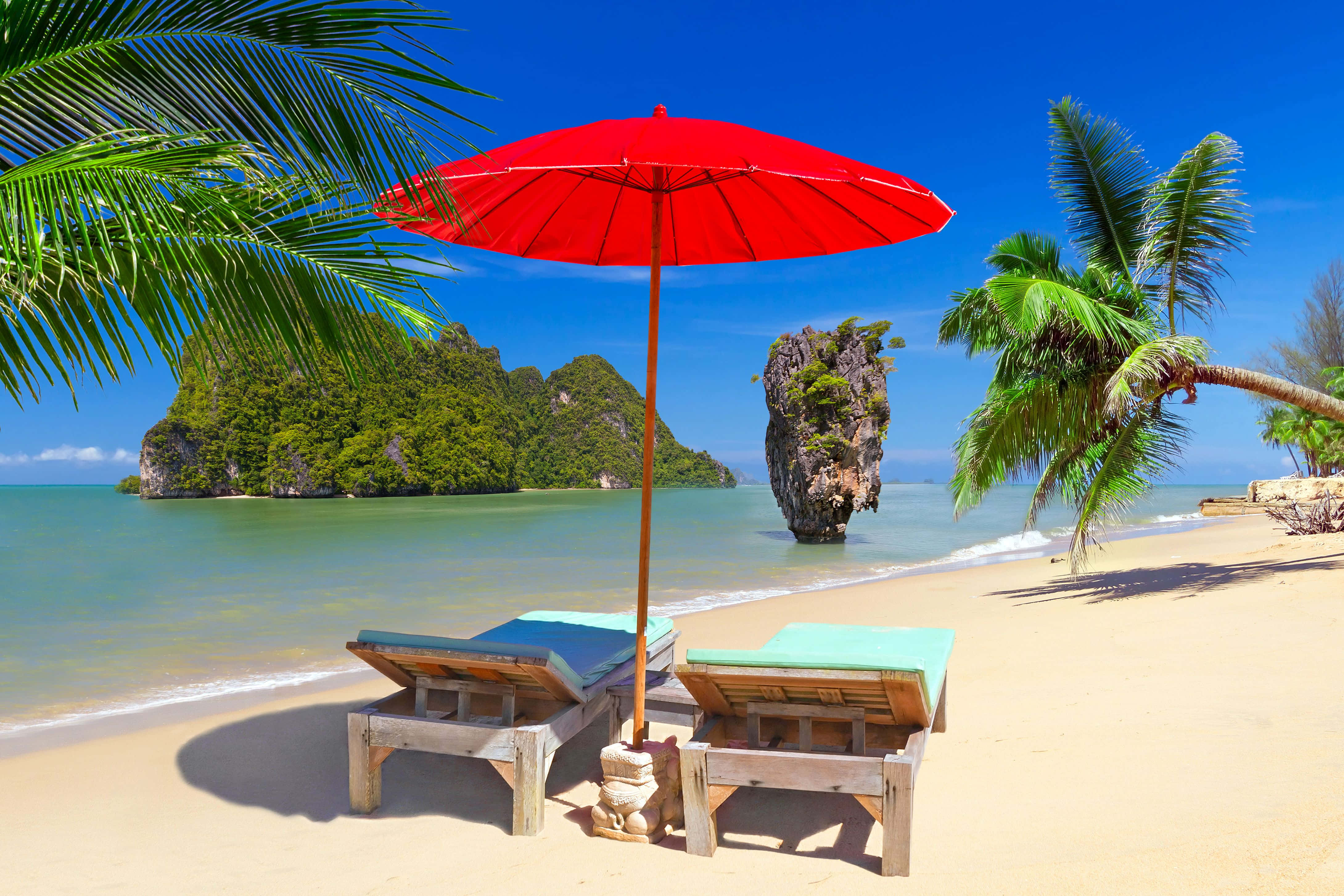 Beach Umbrella 桌布 壁紙 — 兩張木製躺椅在鮮紅色遮陽傘下，金色沙灘、碧綠海水、翠綠喀斯特島嶼，清澈藍天。