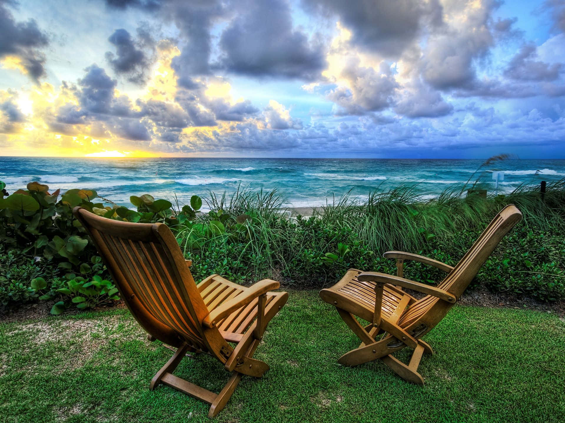 Relaxing 桌布 壁紙 — 兩張木製躺椅面向日落時分充滿活力的綠松石色海洋，伴隨著戲劇性的雲層和拍岸的海浪。