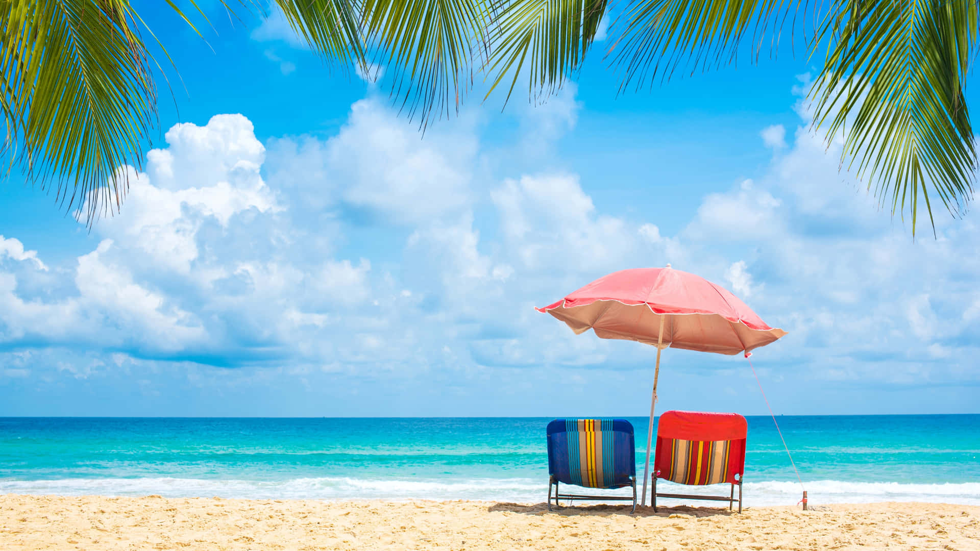 Tropical Beach Chairs Under Palm Trees 壁紙 — 兩張條紋沙灘椅放在粉紅色遮陽傘下，位於金色沙灘上，周圍環繞棕櫚葉，背景是碧綠海洋和晴朗藍天，點綴著蓬鬆白雲。
