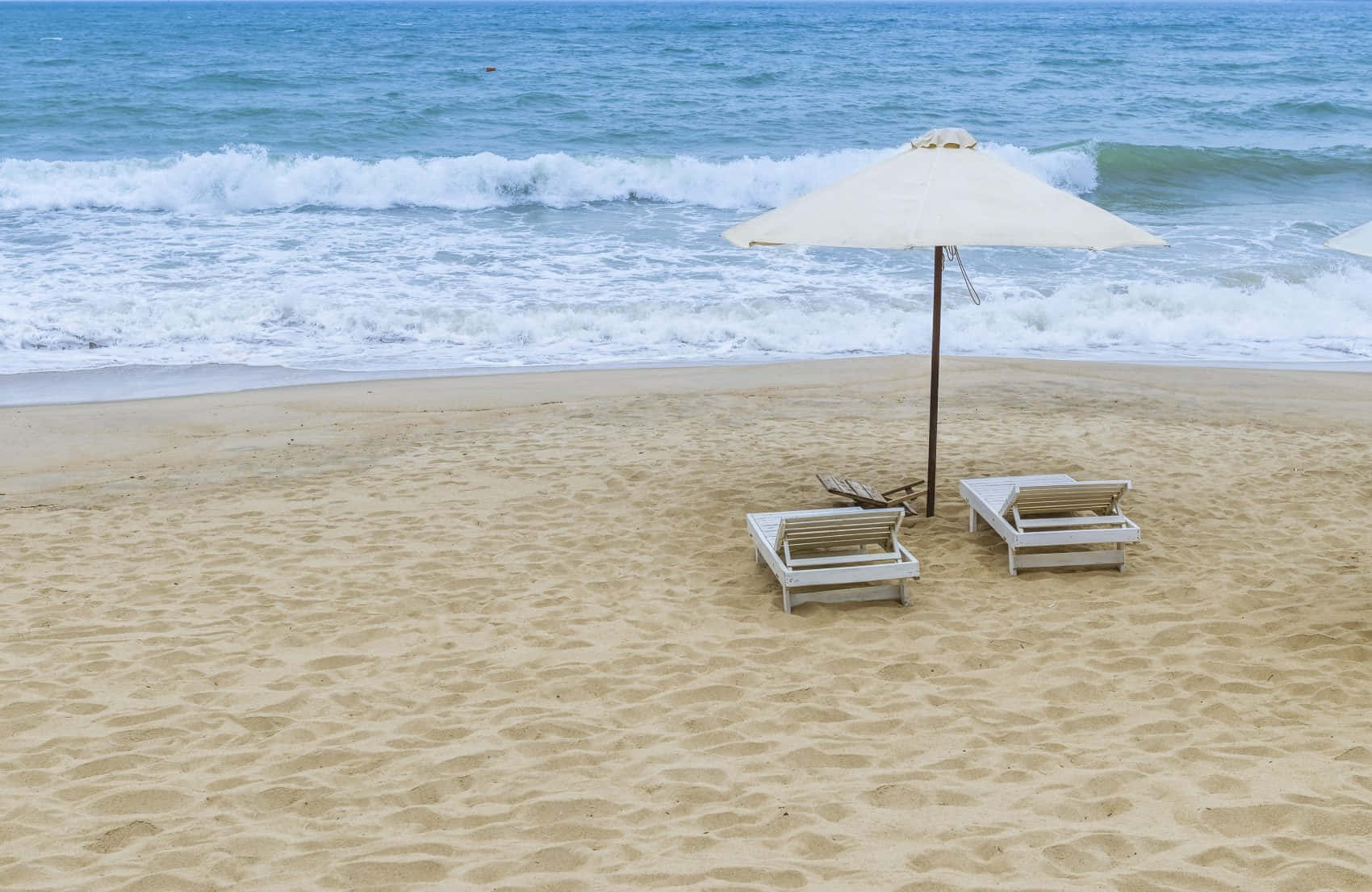 Beach Sunbed 桌布 壁紙 — 兩張白色沙灘椅放在沙灘上的米色遮陽傘下，背景中海浪拍打。