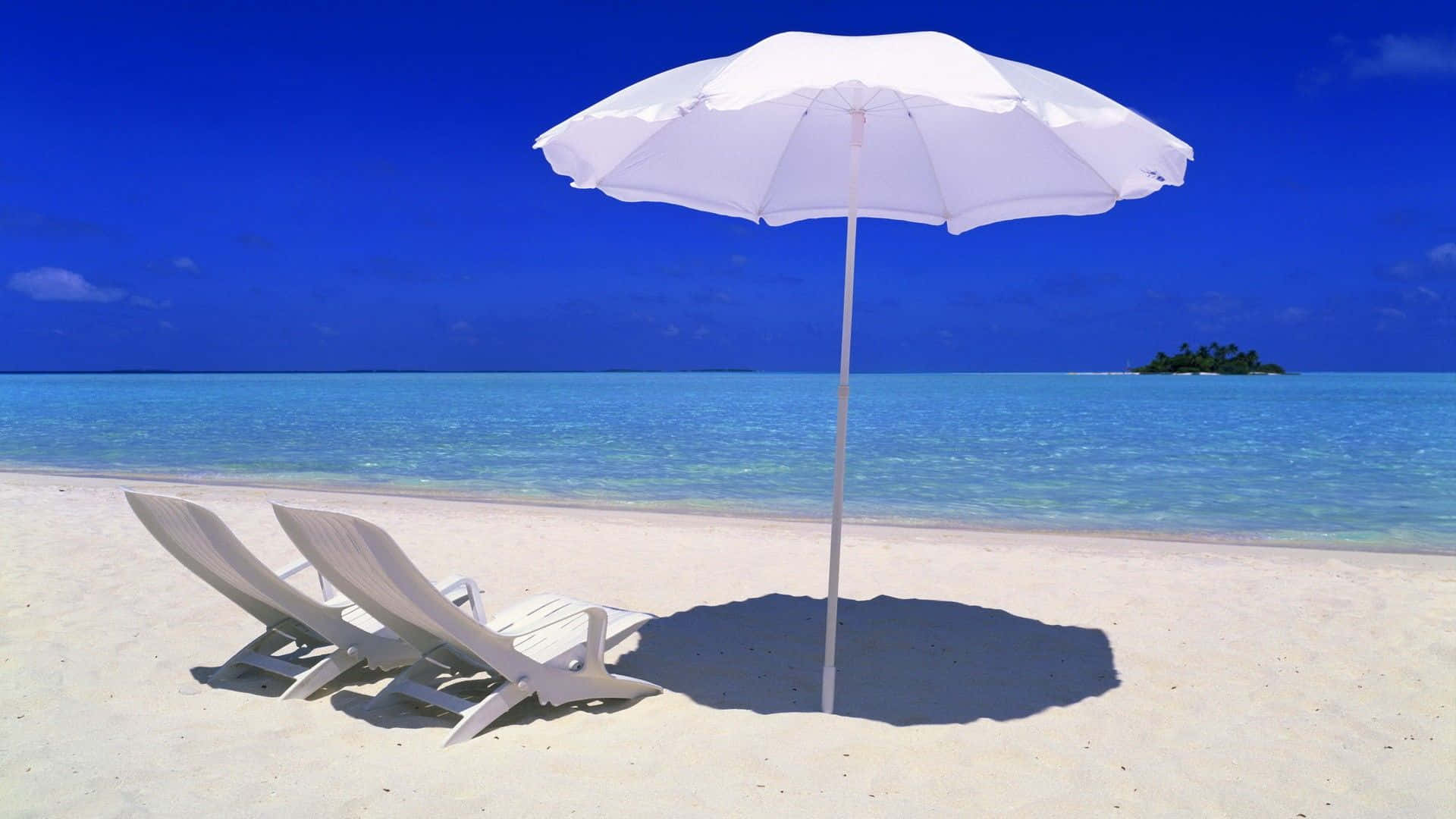Beach Umbrella 桌布 壁紙 — 兩張白色躺椅放在白色遮陽傘下，位於純淨沙灘上，面向碧綠海水和遠處的熱帶島嶼。