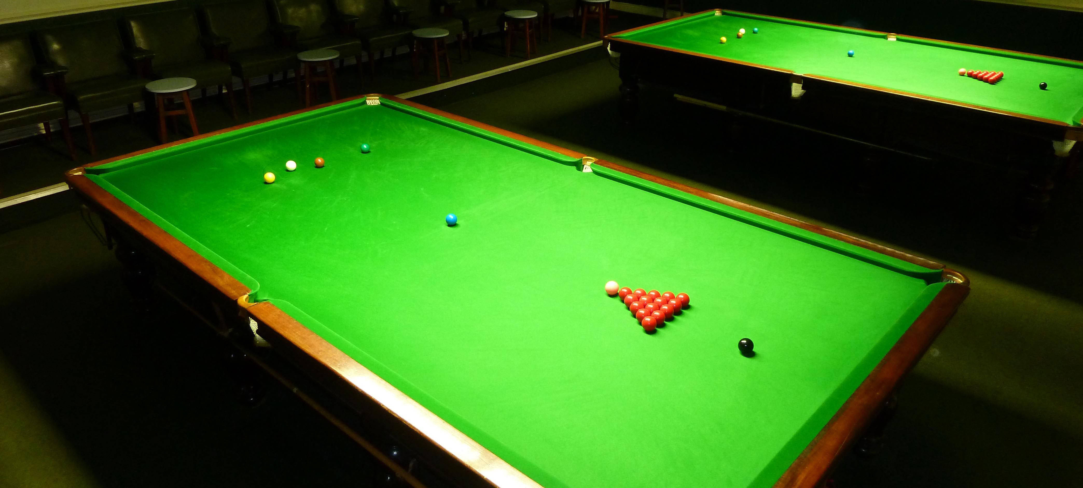 Snooker 桌布 壁紙 — 兩張綠色絨面桌布、球桿排列整齊的司諾克球桌，置於燈光昏暗的寧靜房間內。
