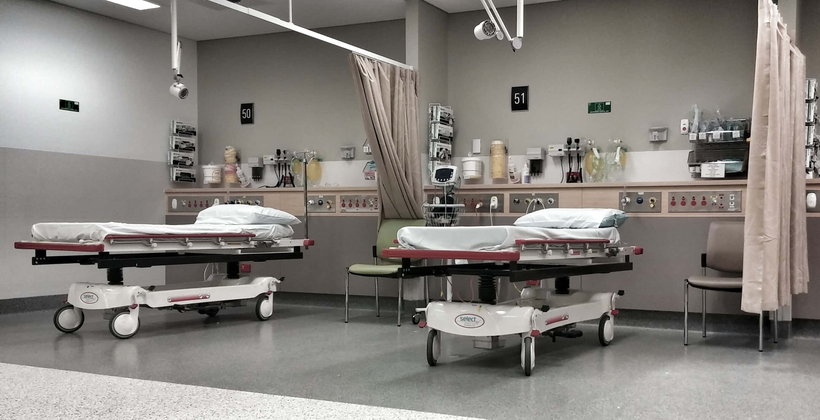 Hospital 桌布 壁紙 — 兩張醫院擔架床放置在一個無菌的急診室隔間內，配有醫療設備和編號的簾子。