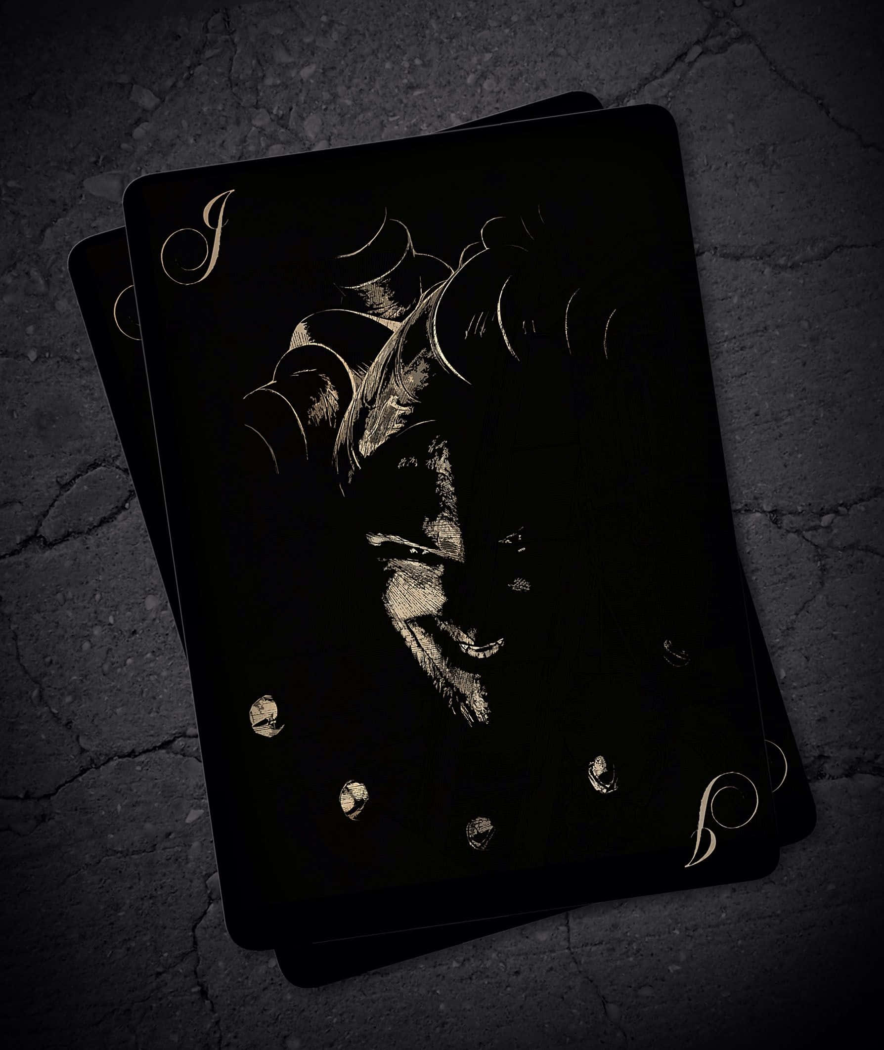 Joker Card 桌布 壁紙 — 兩張黑色撲克牌帶有金色傑克插圖，在昏暗燈光下放置於裂開的混凝土上。